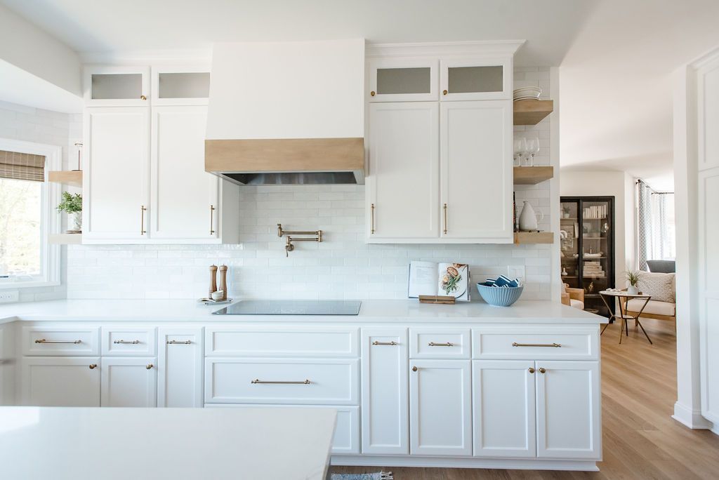 Bright white kitchen with marble counters, white cabinets, and a light wood range hood in a modern home