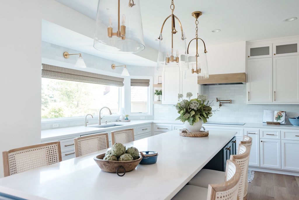 Bright modern kitchen with white island, pendant lights, large window, and potted plant on counter