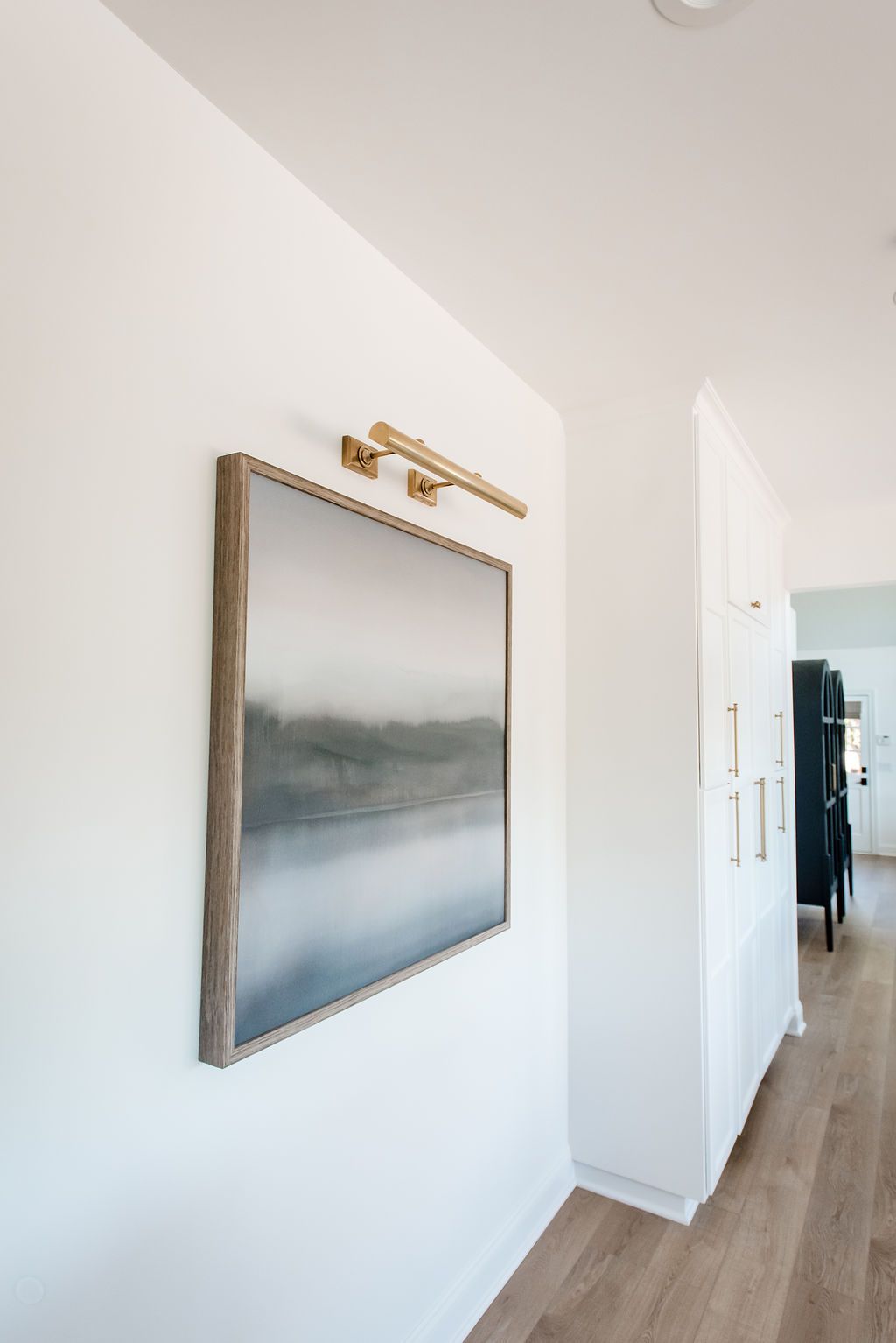 Hallway wall with framed landscape art and brass light fixture in a bright modern interior