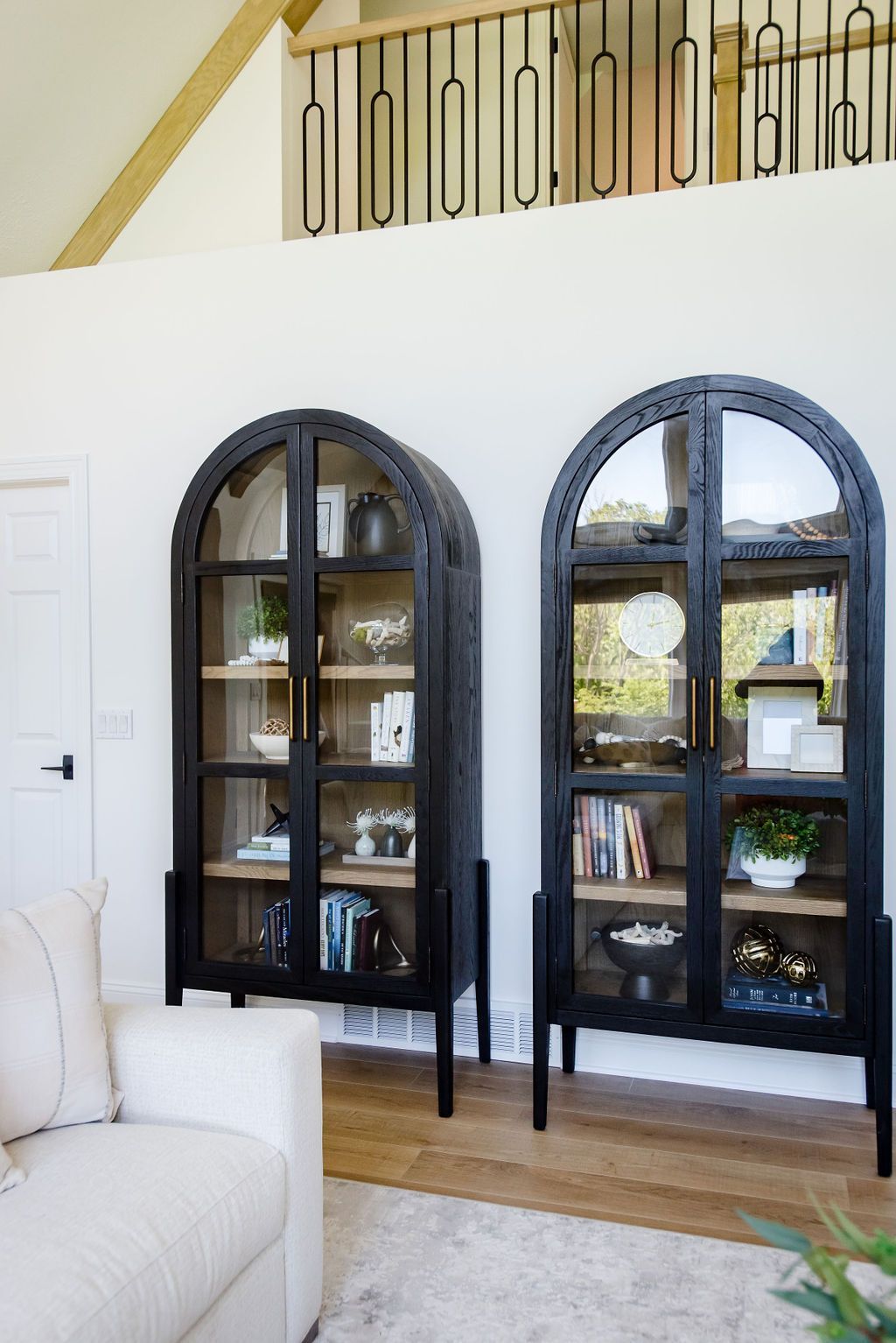 Two black arched display cabinets against a white wall in a bright living room.