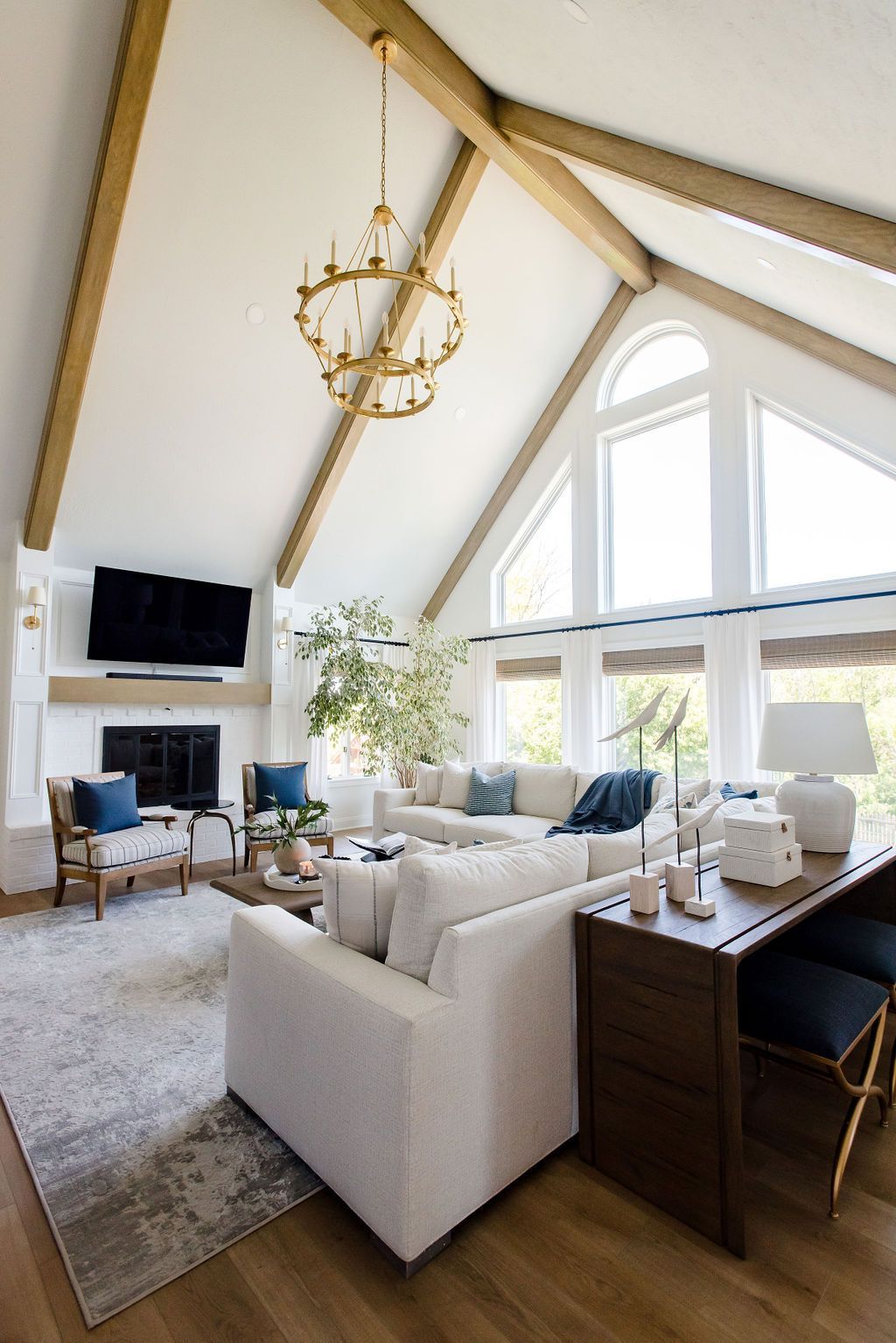 Bright living room with vaulted ceiling, large arched windows, white sofa, fireplace, and gold chandelier.