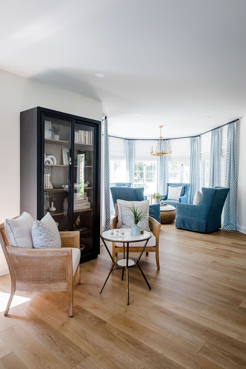 Bright living room with wicker chairs, blue sofa, black cabinet, and large windows with curtains