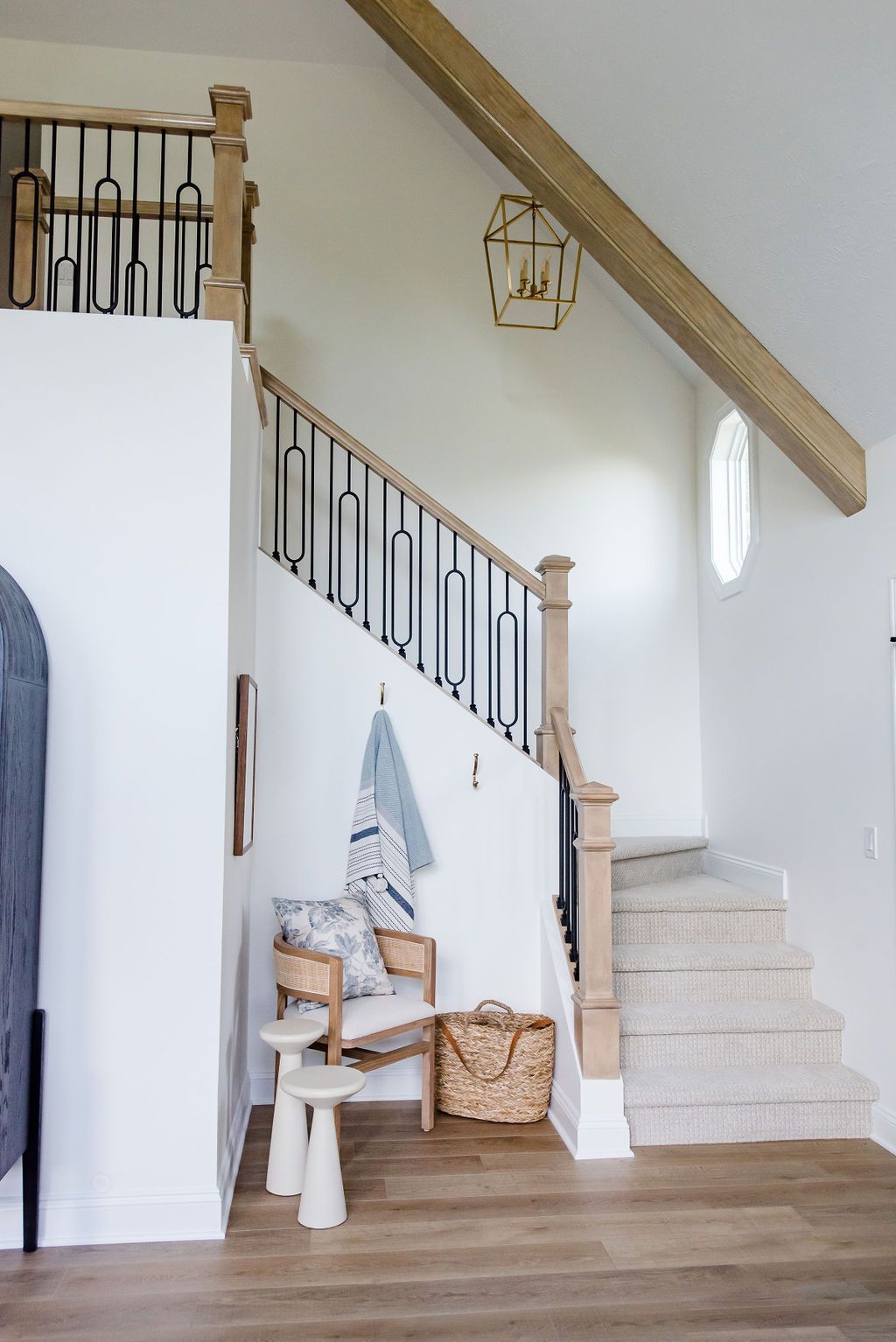 Staircase with white walls, wood banister, woven baskets, and a small chair in a bright hallway