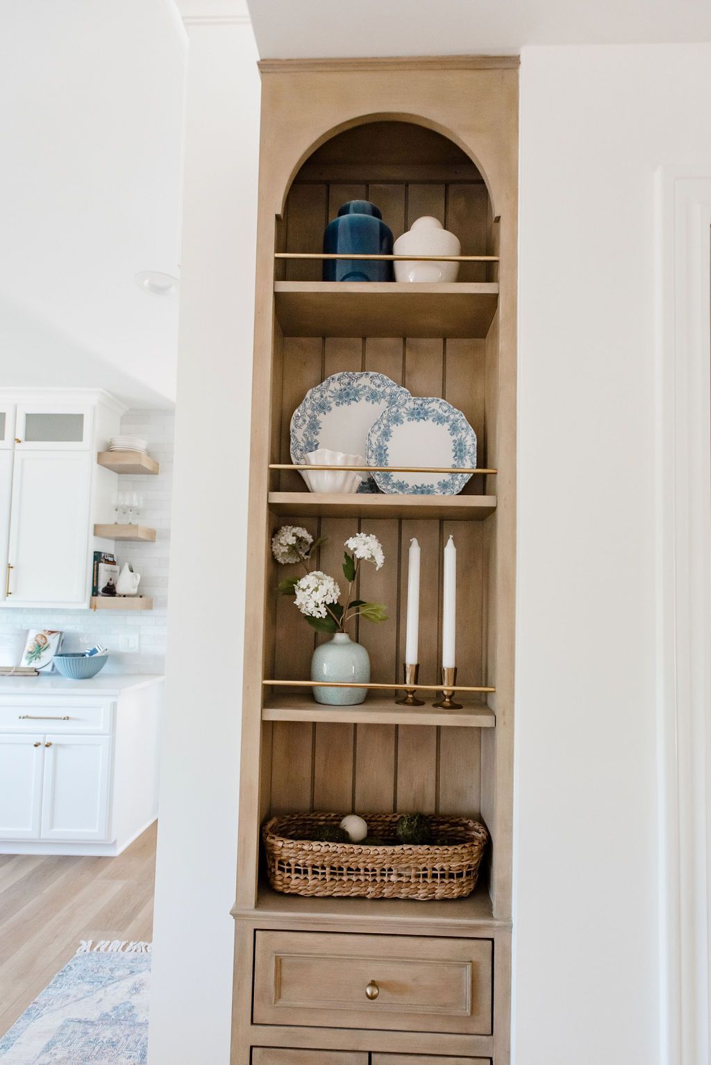 Built-in wood shelving with blue-and-white plates, vases, flowers, and a wicker basket in a hallway