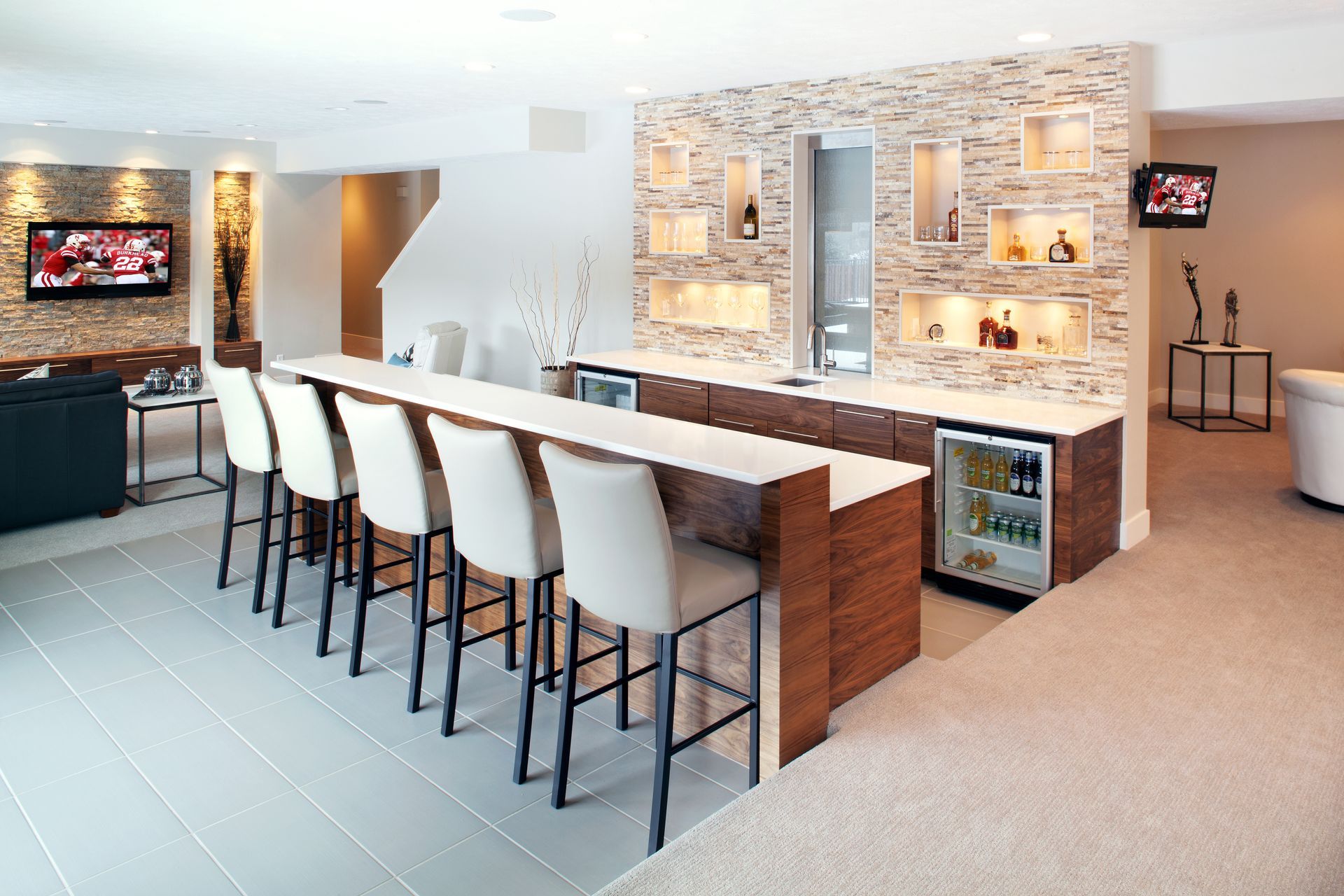 Modern kitchen and bar with a long island, white stools, stone accent wall, and carpeted lounge area