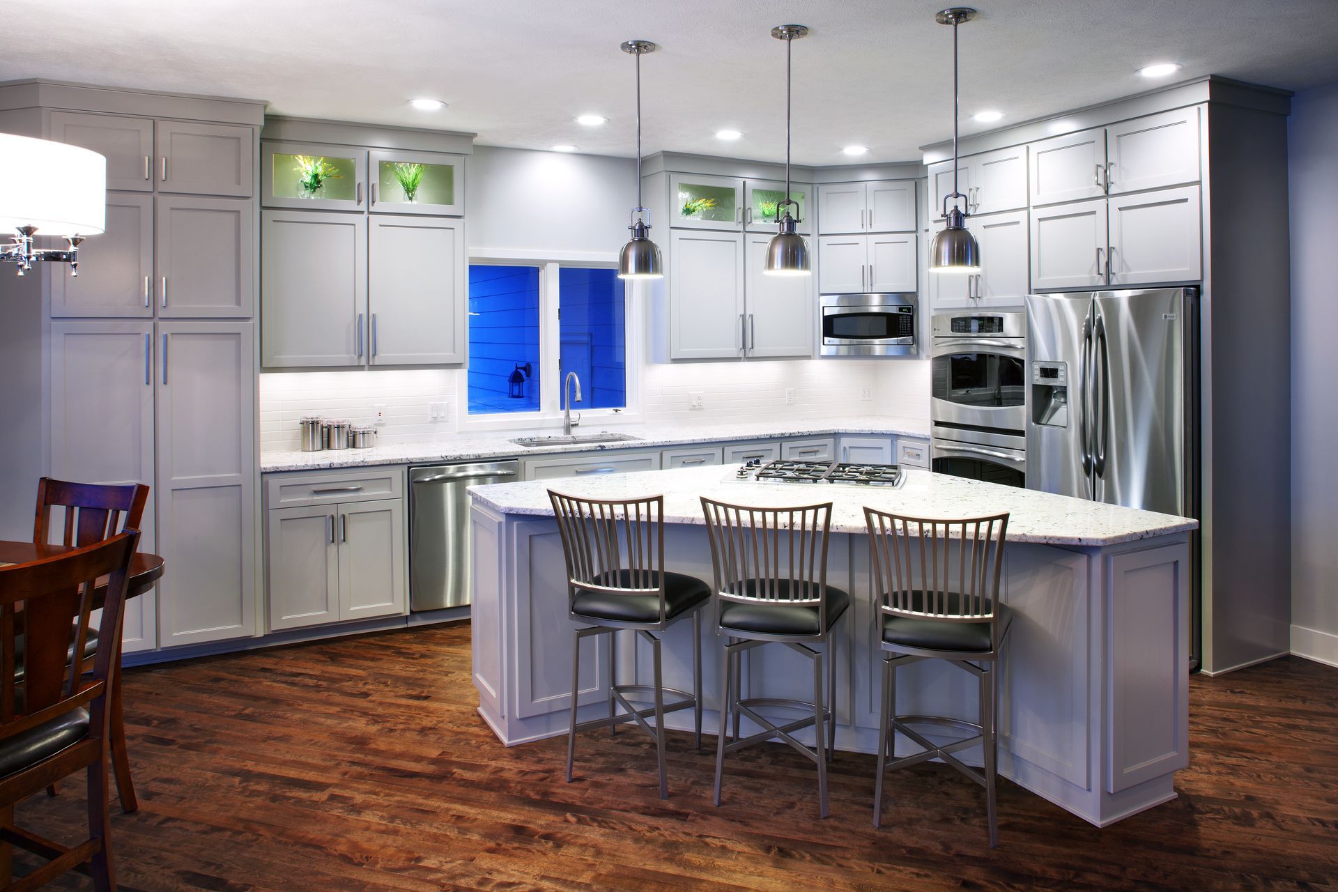 Modern white kitchen with island, stainless steel appliances, and three bar stools