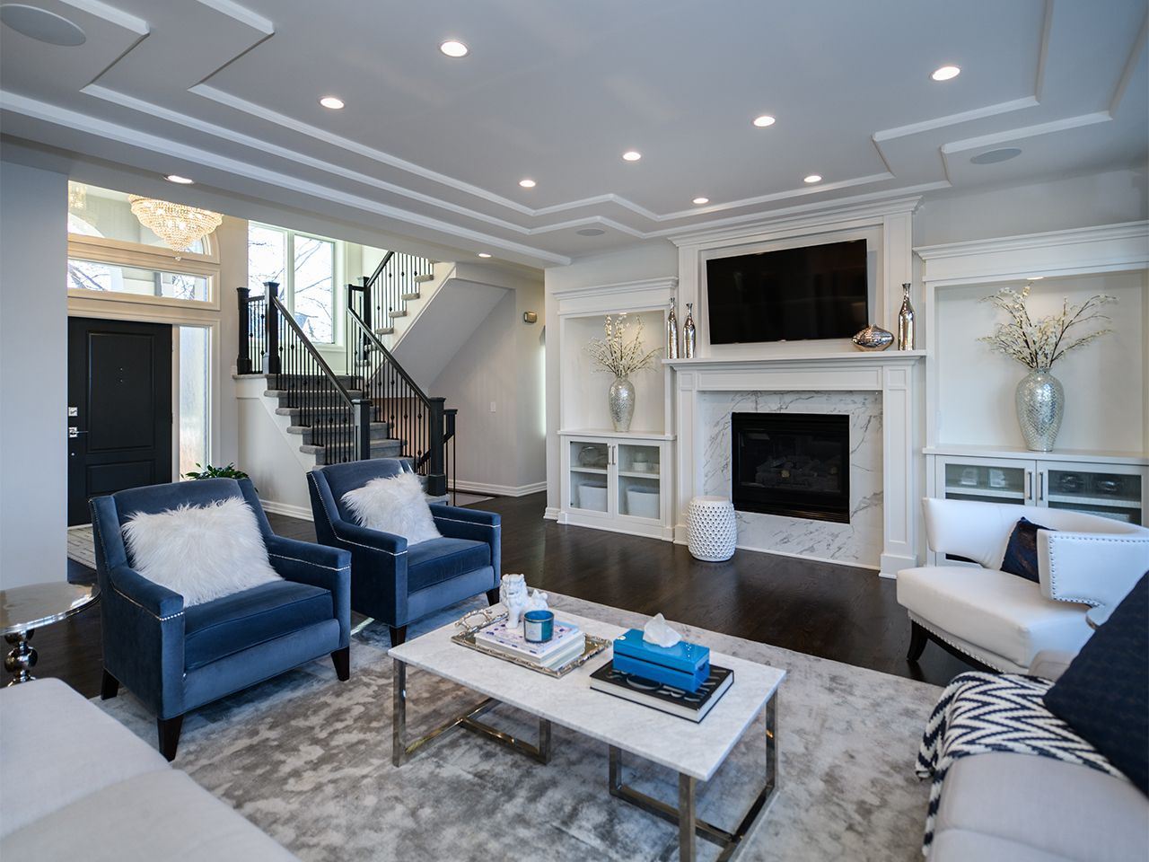 Bright modern living room with blue chairs, white fireplace, and large windows