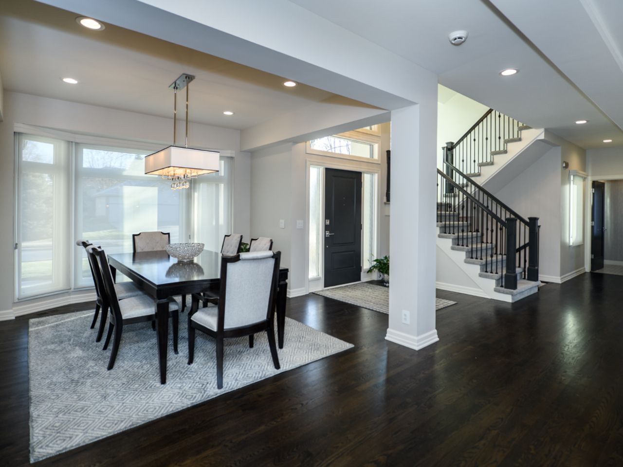 Modern dining room with black chairs, chandelier, and staircase in a bright open foyer