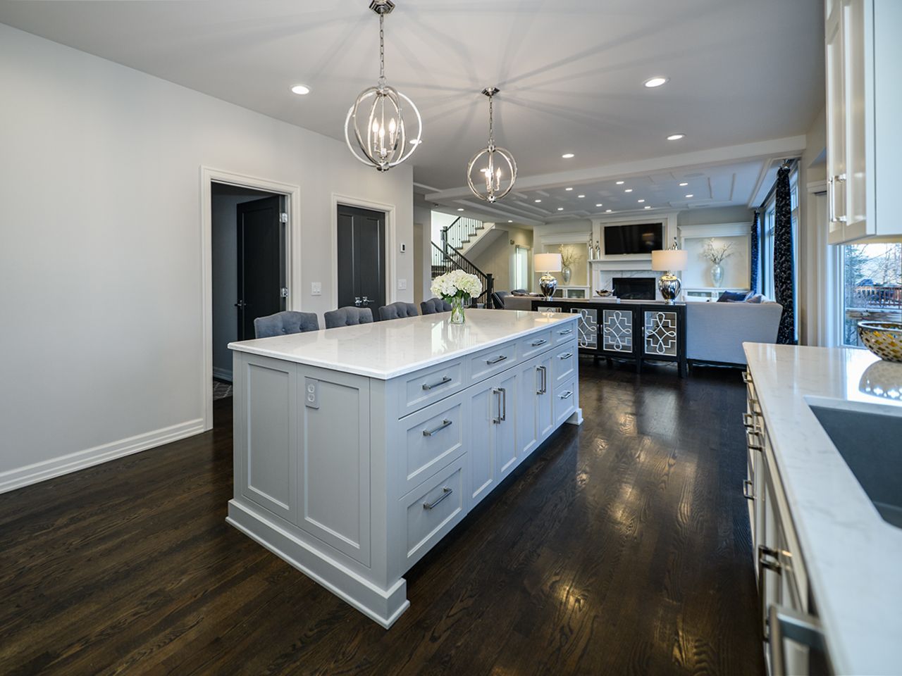 Modern white kitchen with a large island, dark wood floors, and pendant lights