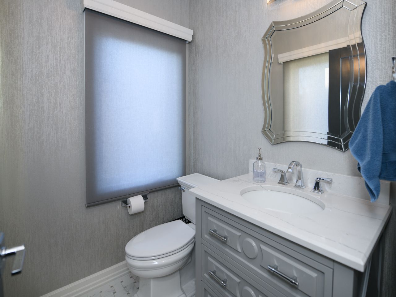 Small bathroom with vanity sink, toilet, window shade, and a mirror above the sink.