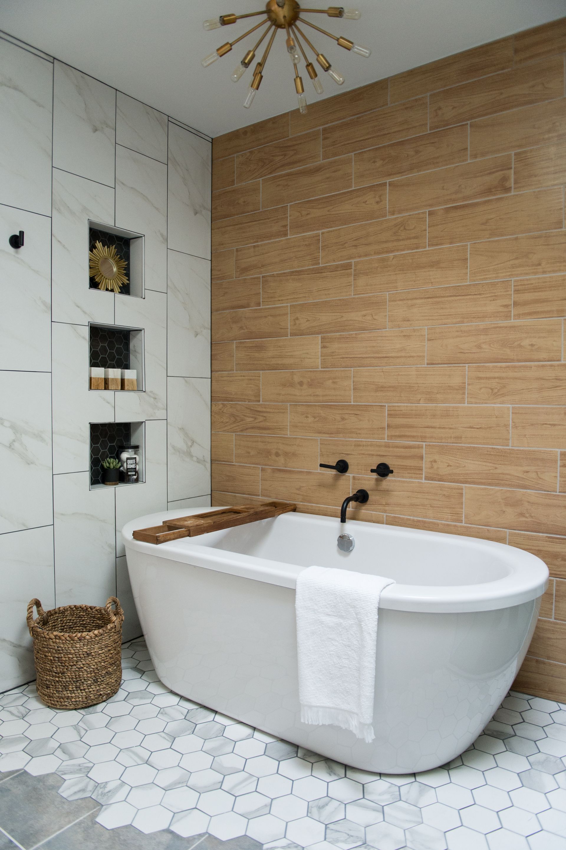 Modern bathroom with freestanding tub, white hex tile floor, wood-look accent wall, and recessed shelves