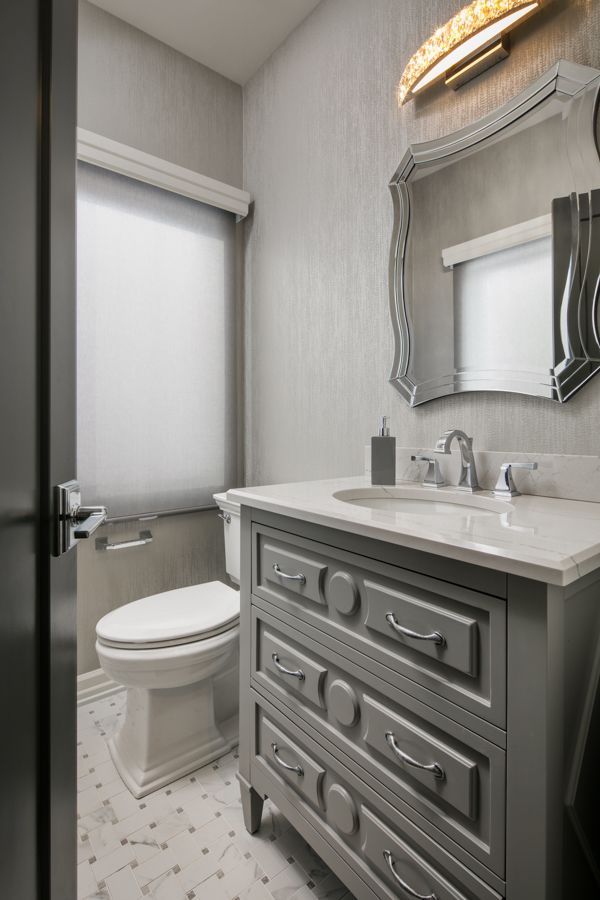 Small bathroom with gray vanity, white sink, mirror, toilet, and patterned tile floor