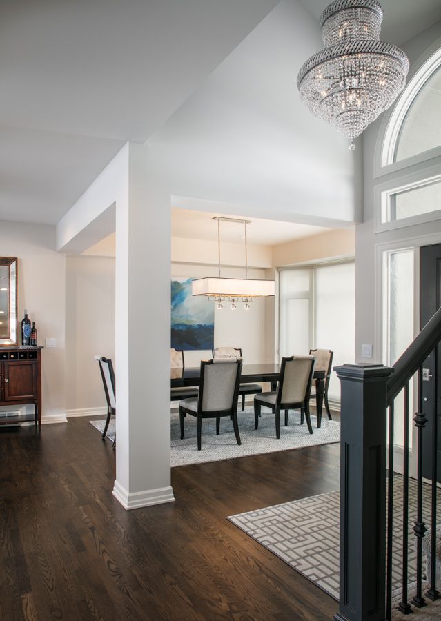 Bright foyer with chandelier, dark wood floors, dining area, and staircase by a large arched window