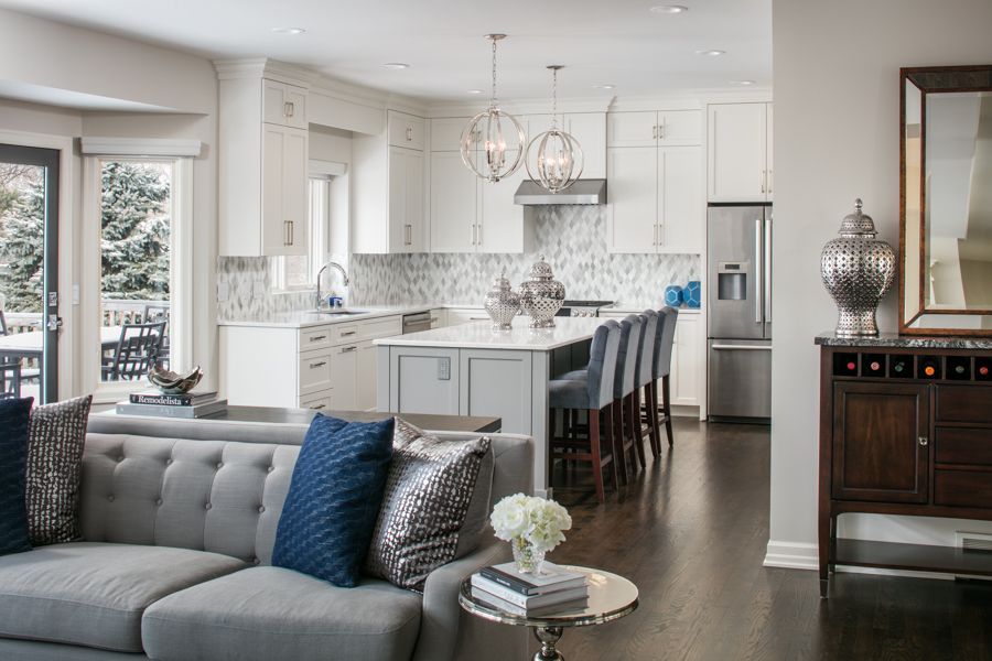 Bright, modern kitchen and living area with white cabinets, gray sofa, and dark wood floors.
