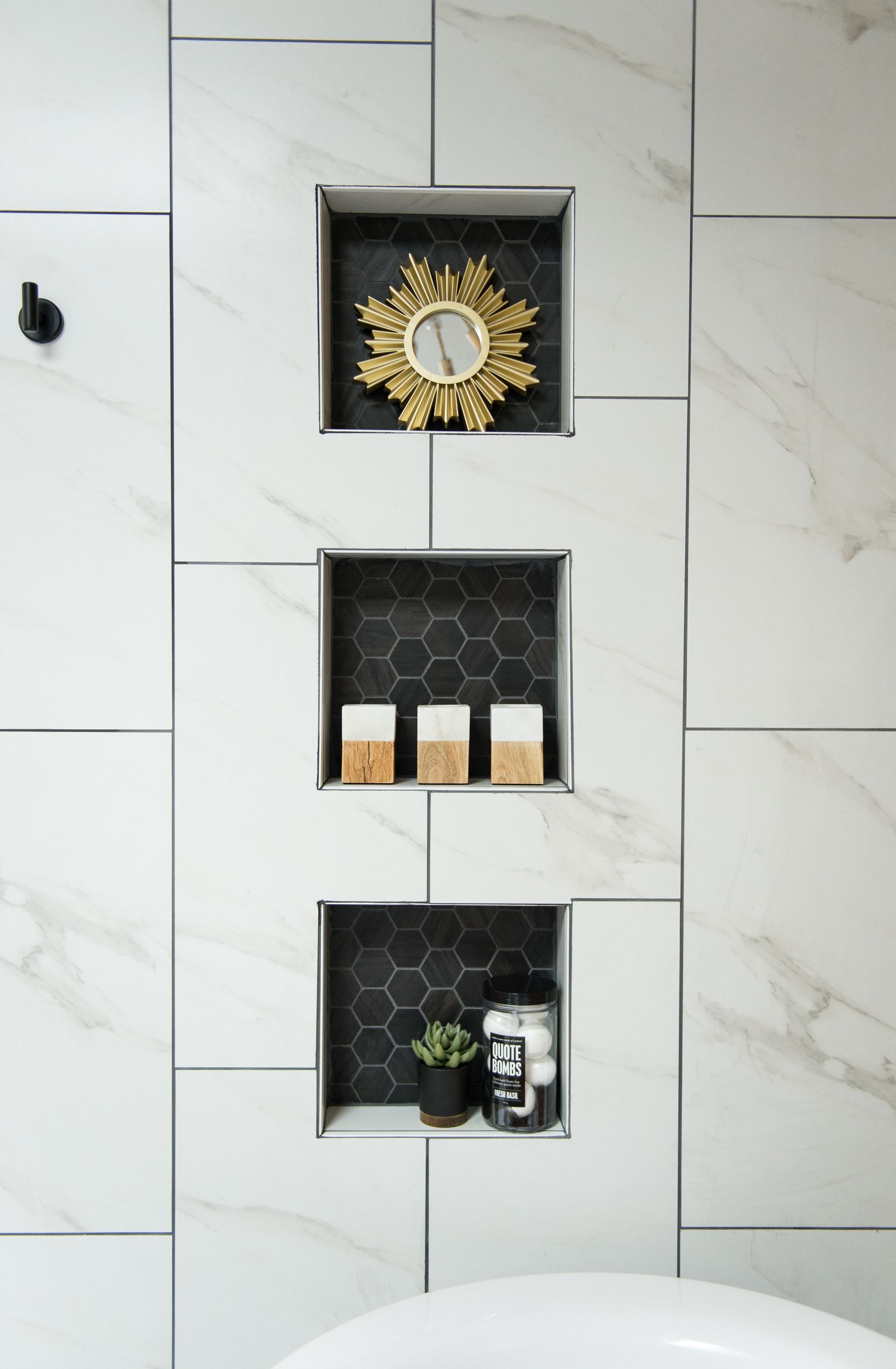 Tiled bathroom wall with three recessed shelves holding a decorative mirror, candles, and toiletries.