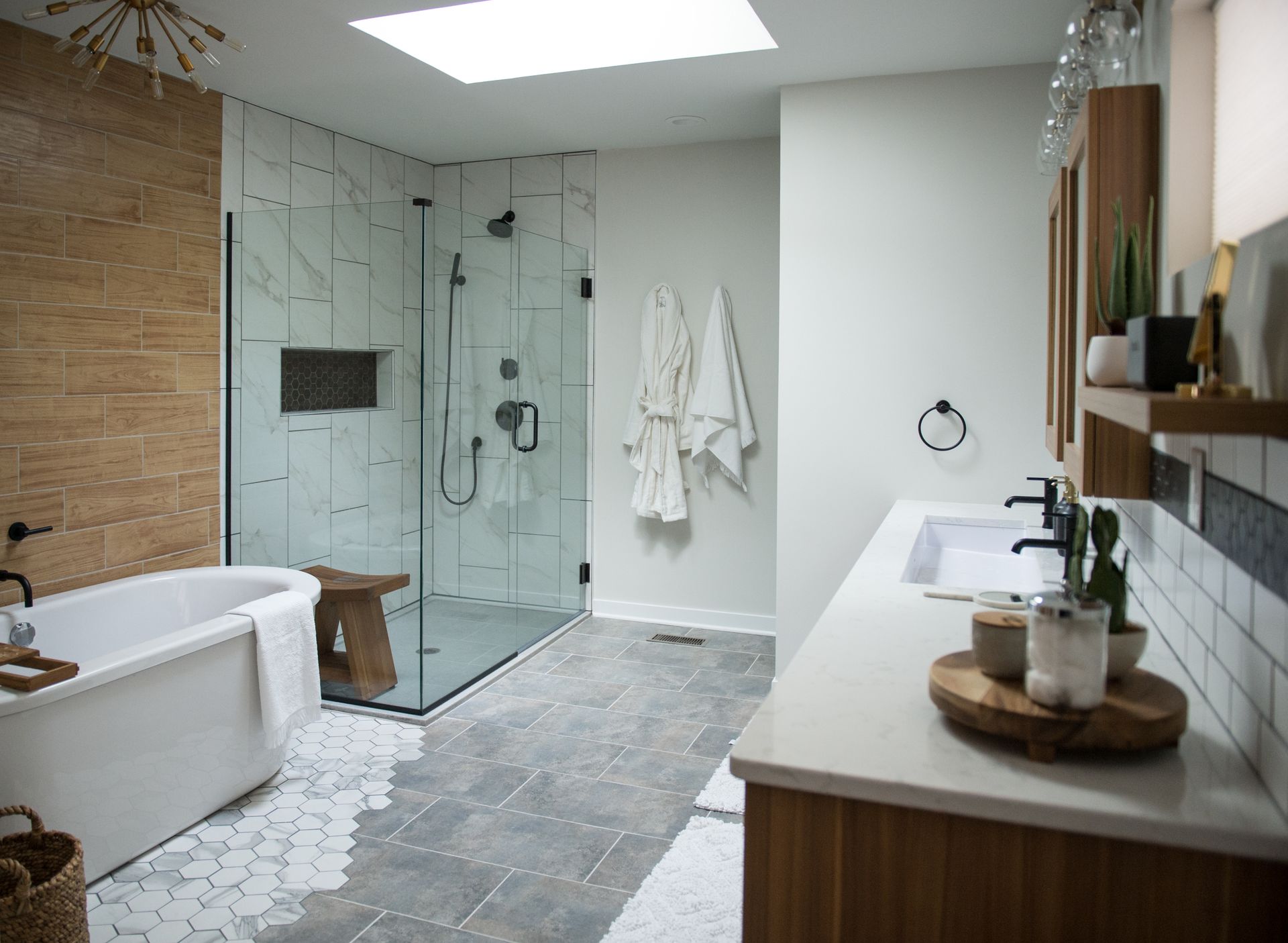 Modern bathroom with glass shower, freestanding tub, double vanity, and gray tile flooring