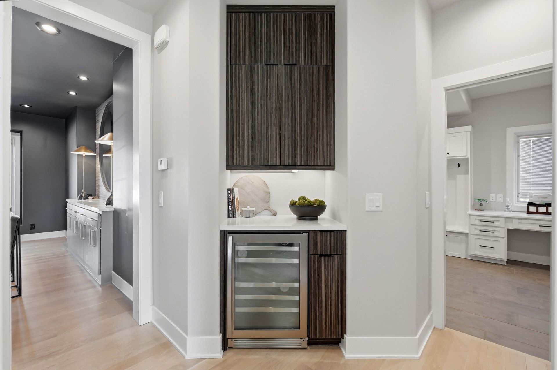 Modern hallway with built-in wine fridge and cabinetry, leading to a bright bedroom and bathroom.