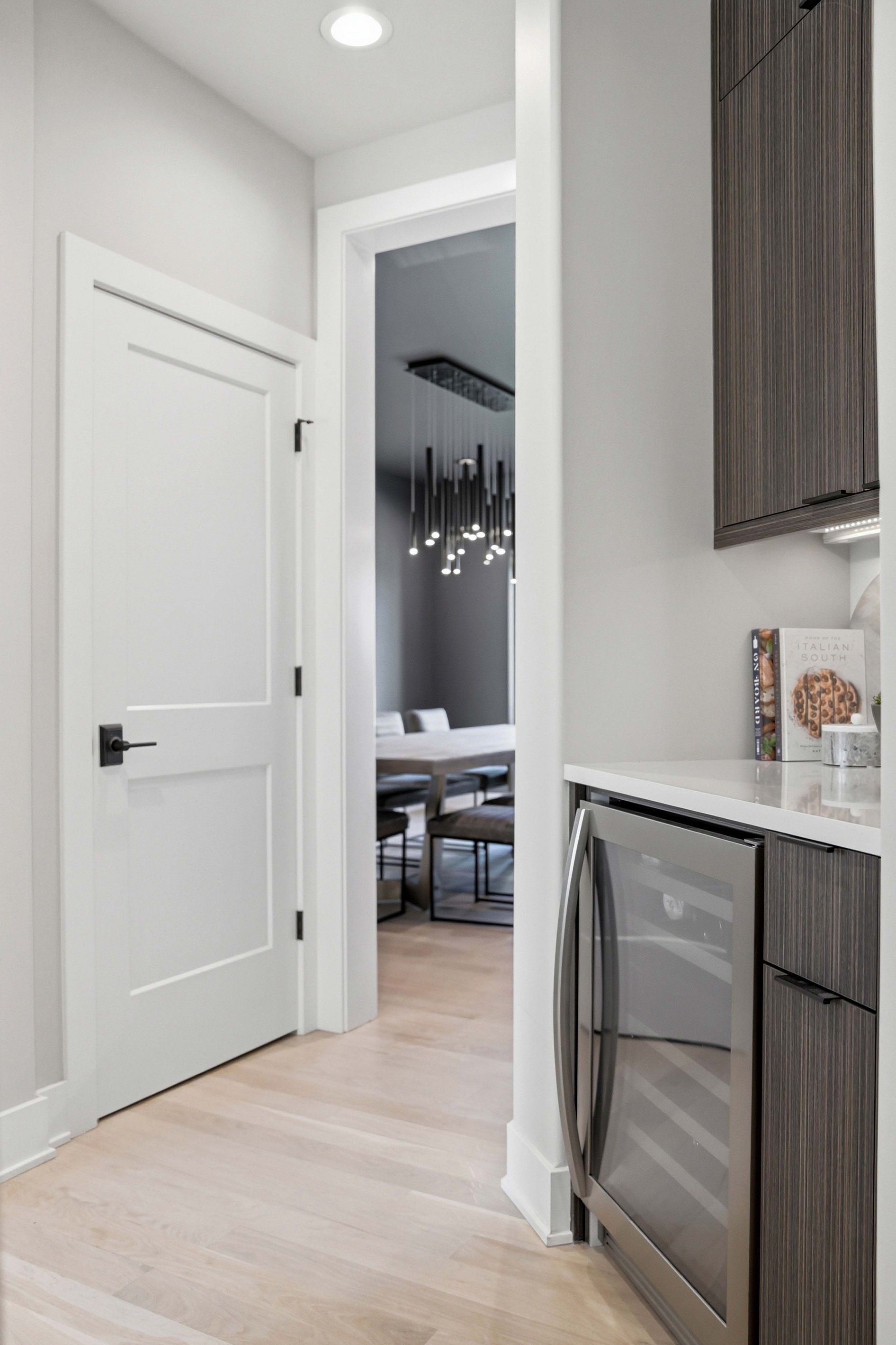 Bright modern kitchen hallway with white door, light wood floor, and stainless steel oven next to dark cabinets