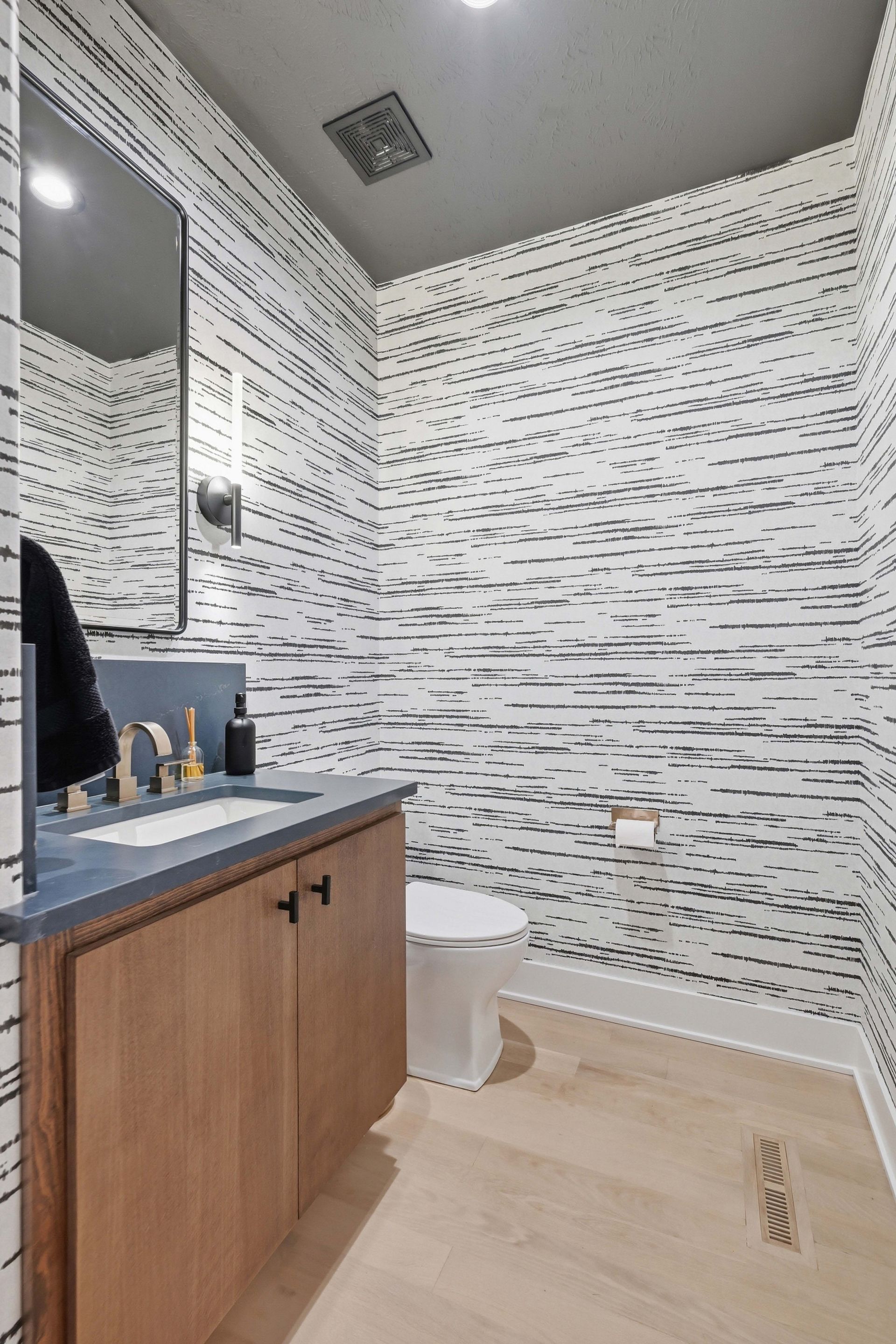 Modern bathroom with wood vanity, white patterned walls, mirror, toilet, and light wood flooring
