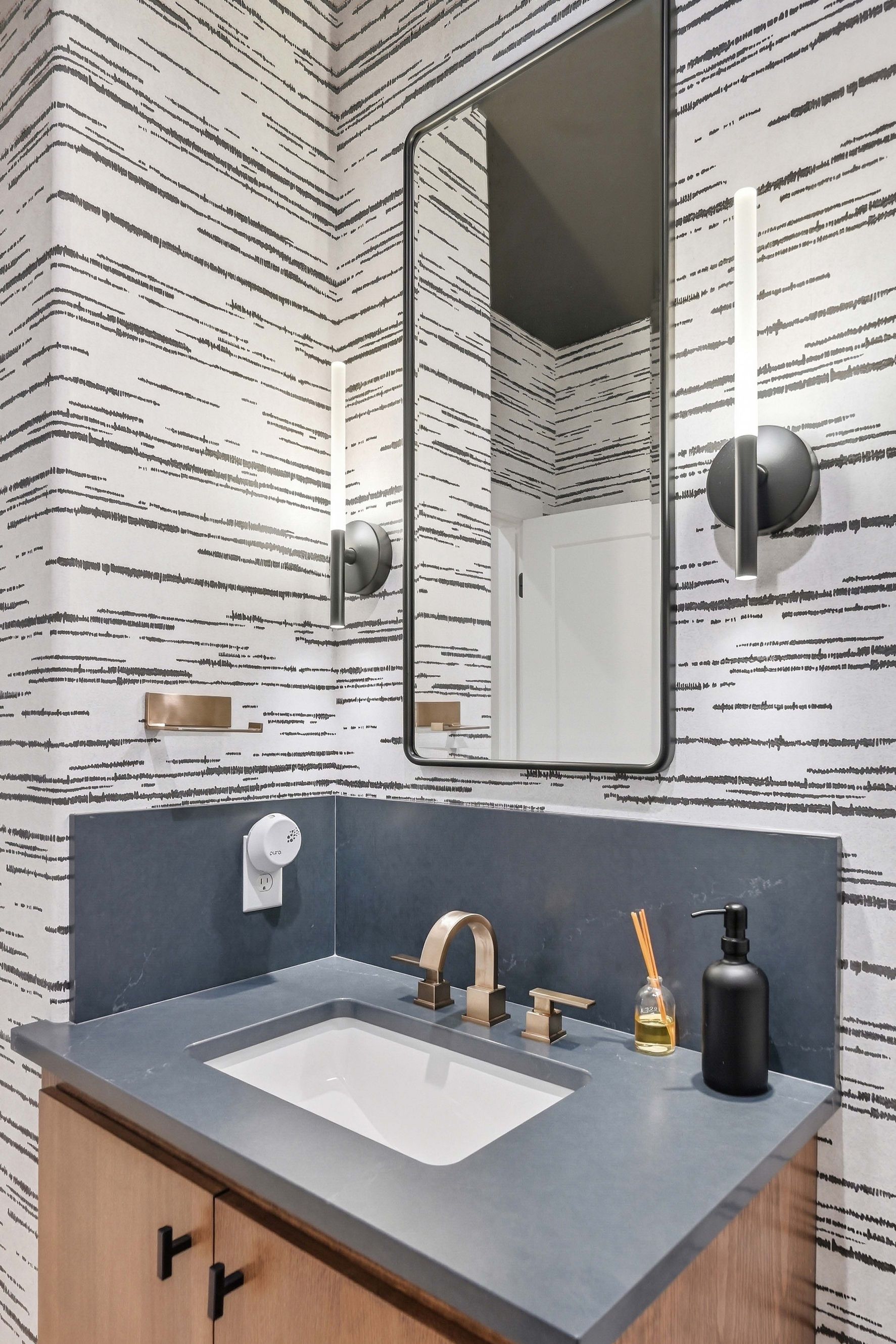 Modern bathroom vanity with gray countertop, sink, gold faucet, mirror, and patterned wallpaper