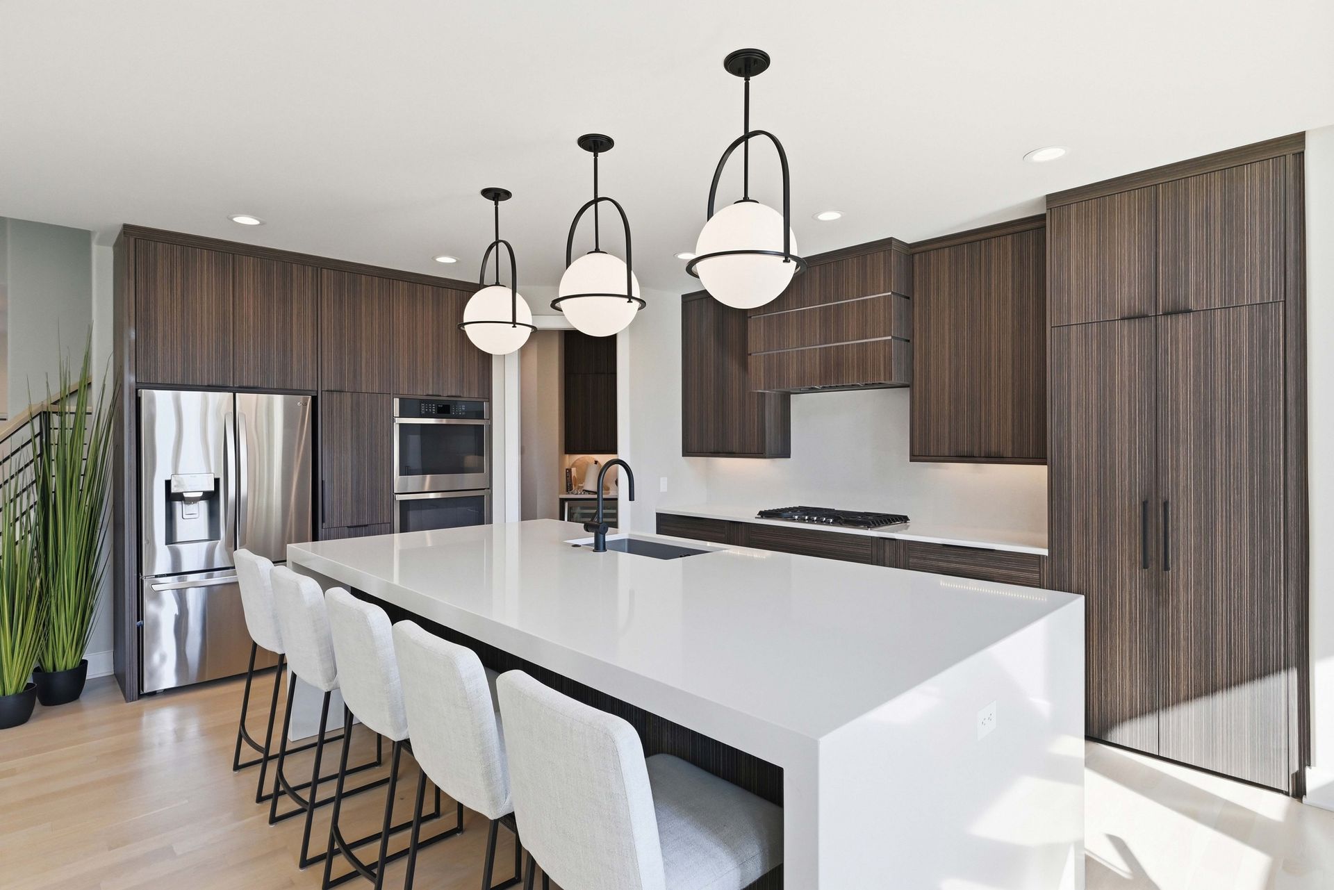 Modern kitchen with white island, black pendant lights, bar stools, and wood cabinetry