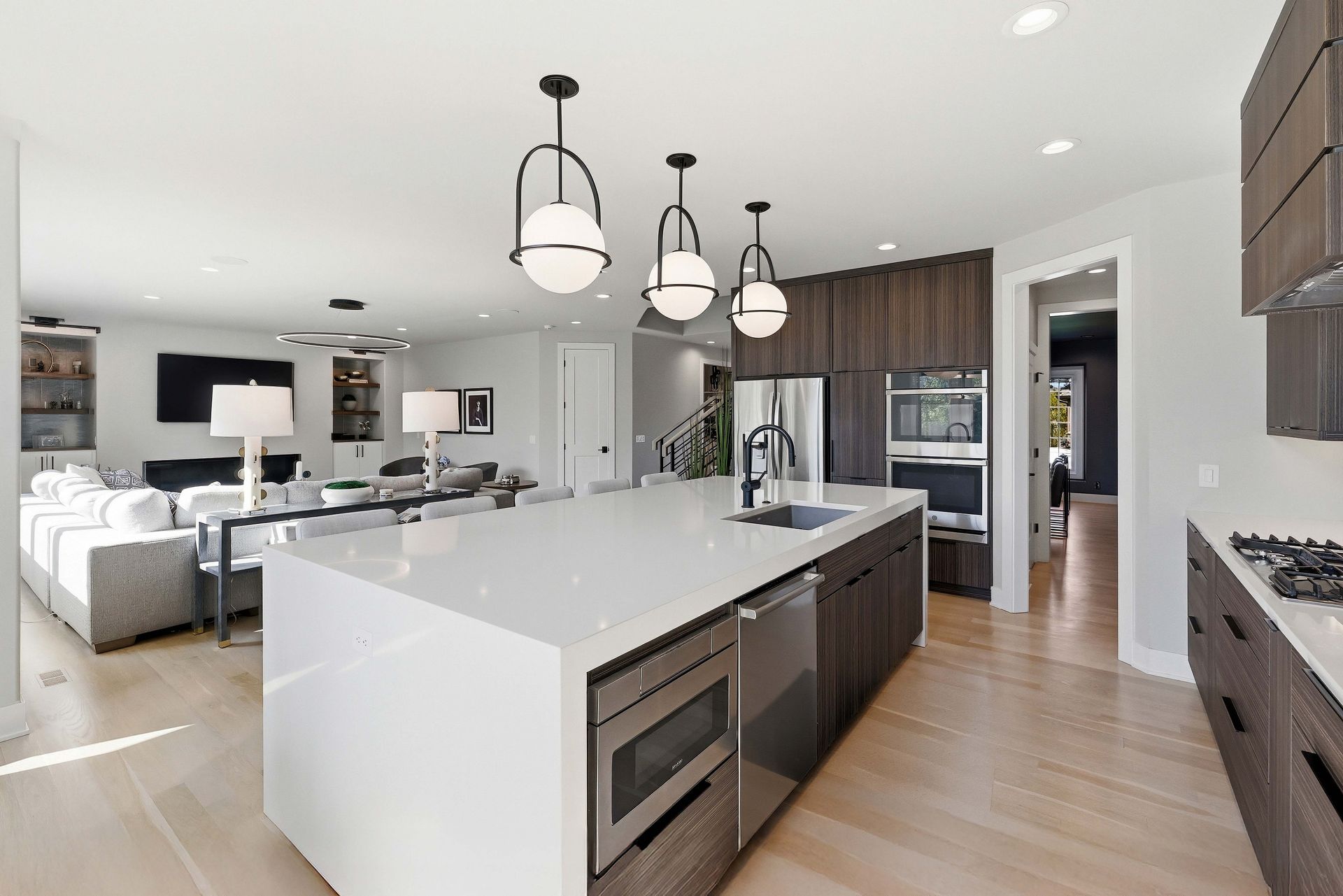 Bright modern kitchen with white island, pendant lights, wood floors, and open living area