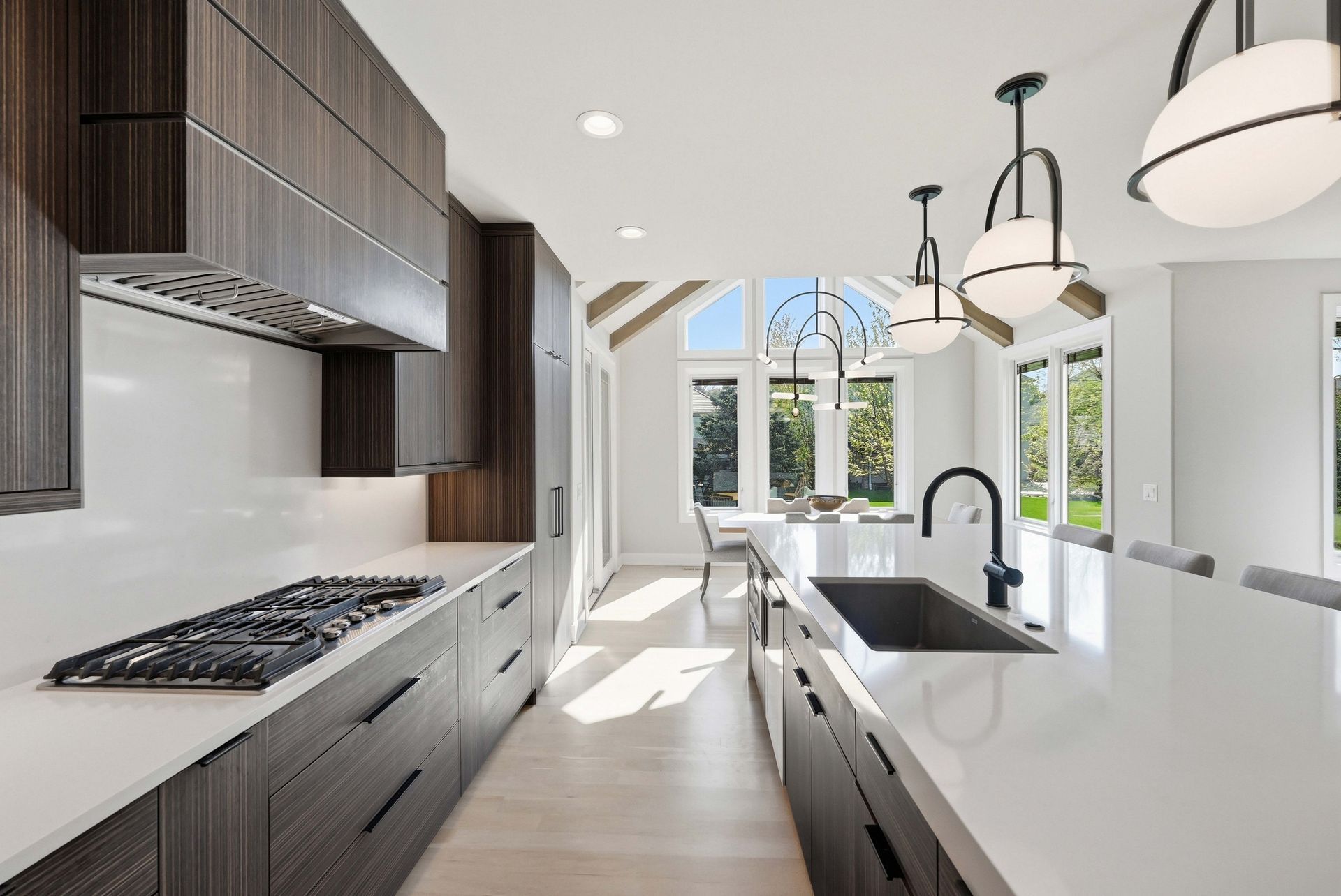 Modern white kitchen with dark wood cabinets, island sink, gas range, and large windows letting in bright light
