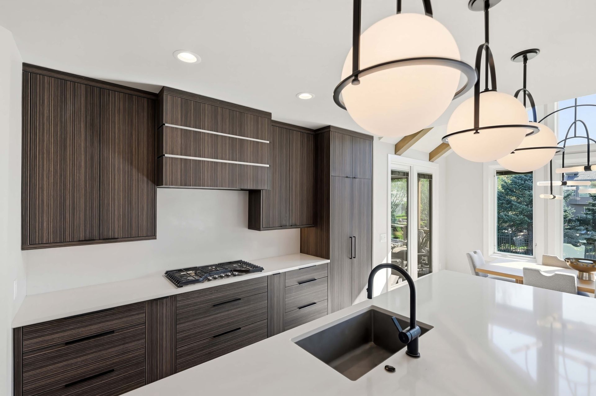 Modern kitchen with dark wood cabinets, white island, pendant lights, and large windows