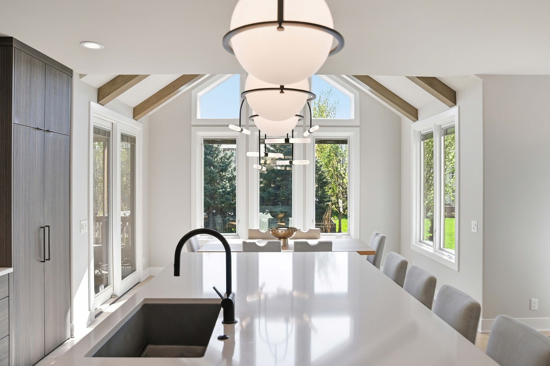 Bright modern kitchen with white island, black faucet, pendant lights, and large windows.