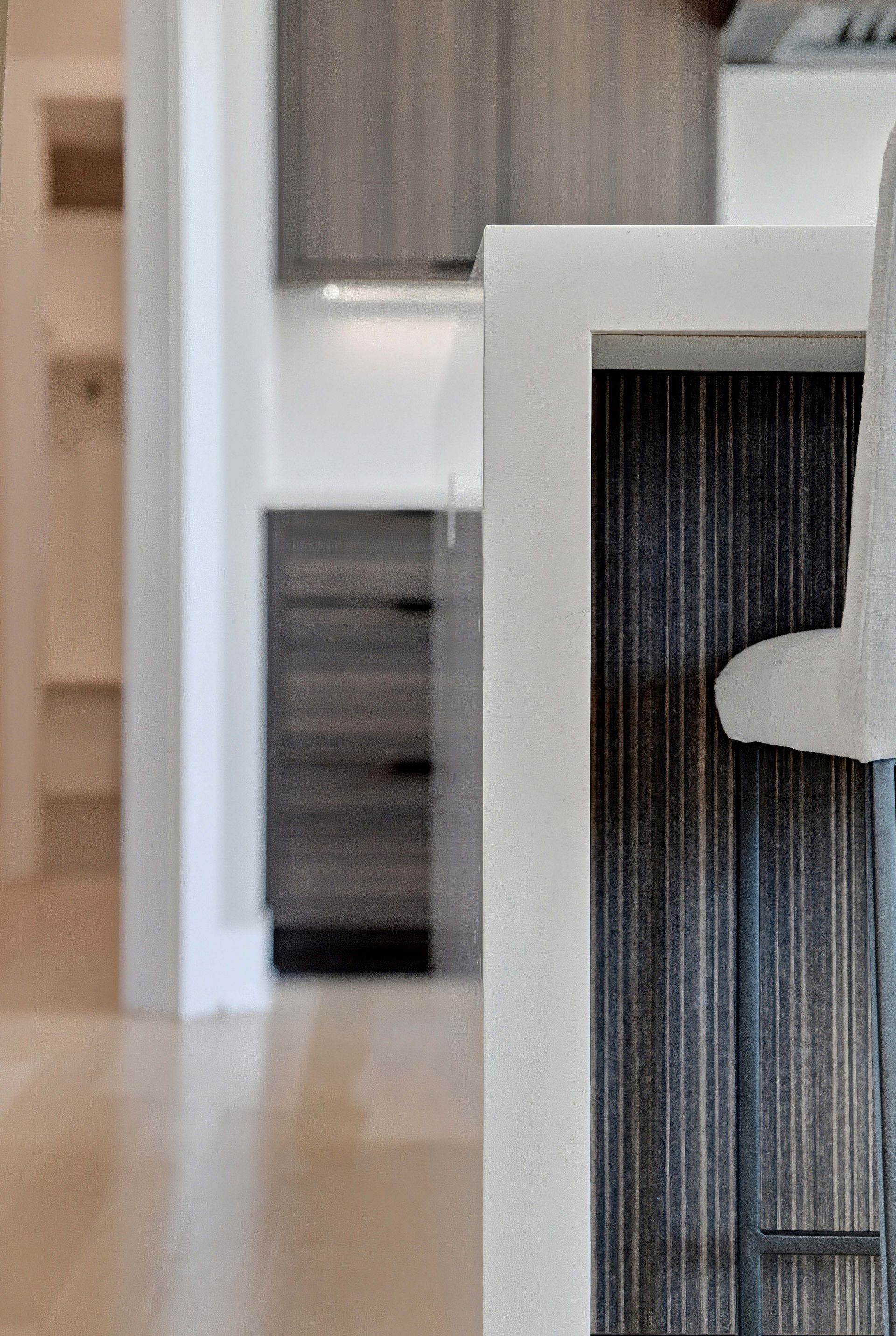 Modern chair in the foreground of a bright hallway with a doorway and cabinet in the background