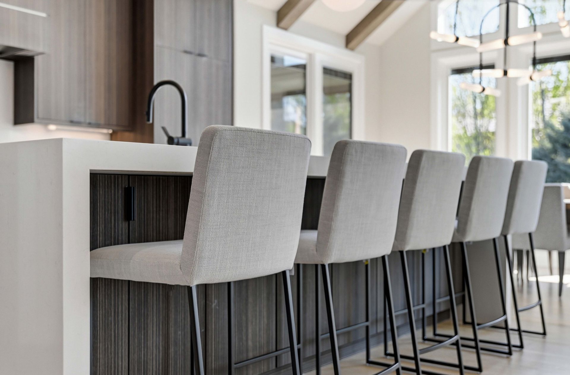 Modern kitchen island with four gray upholstered bar stools and pendant lighting