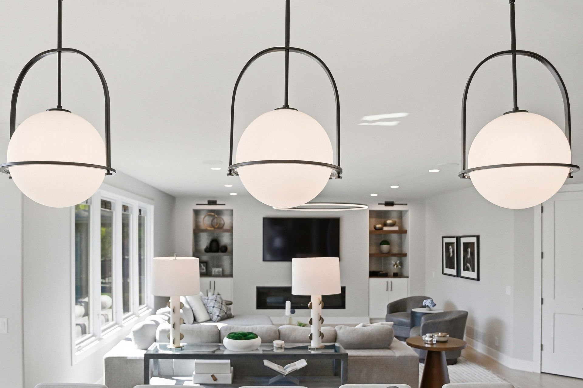 Bright modern living room with white walls, large windows, gray sofa, and three hanging globe lights