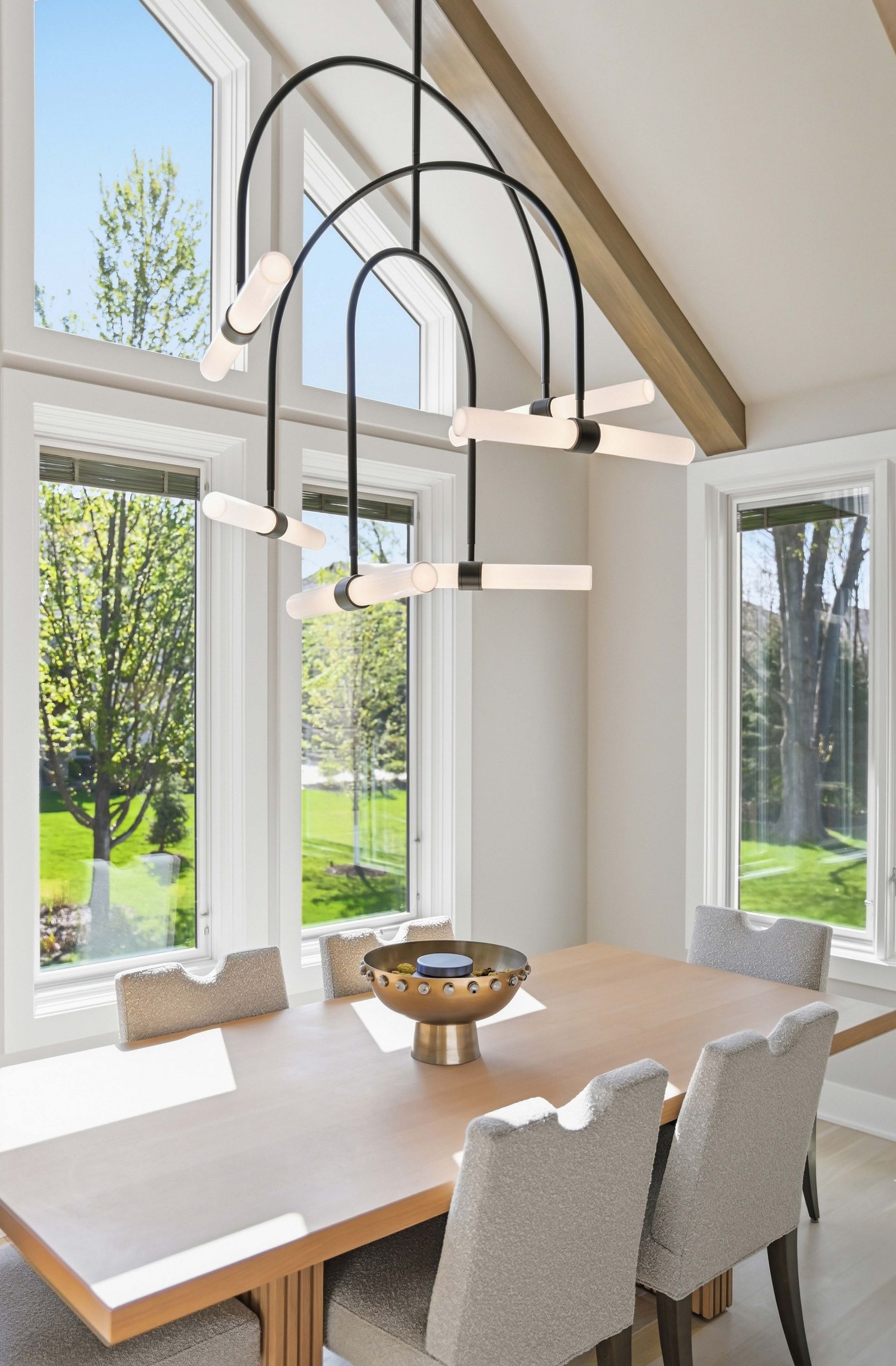 Bright dining room with large windows, white table, upholstered chairs, and modern pendant lights