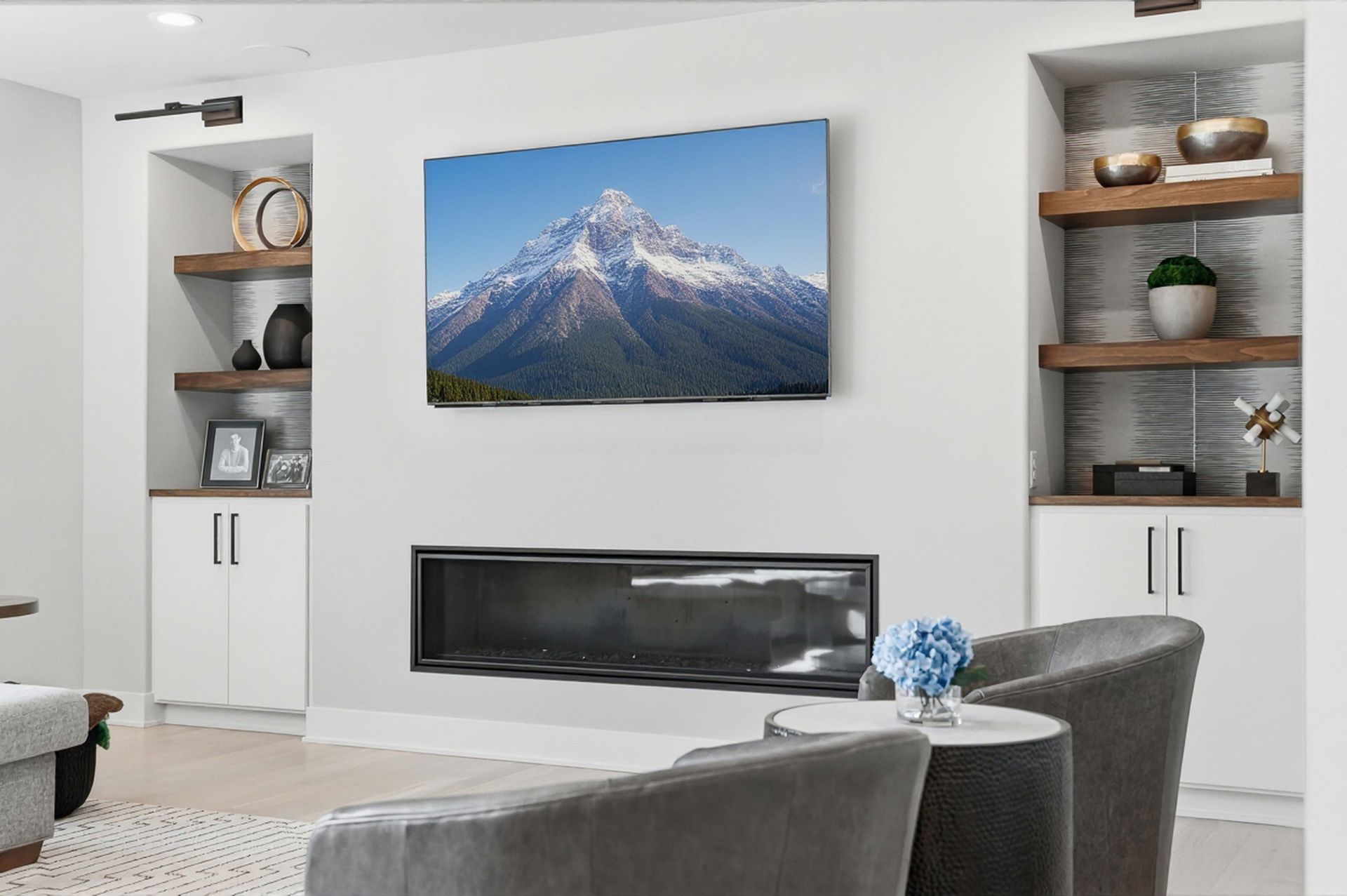 Modern living room with a wall-mounted mountain photo, fireplace, and built-in shelves with decor.