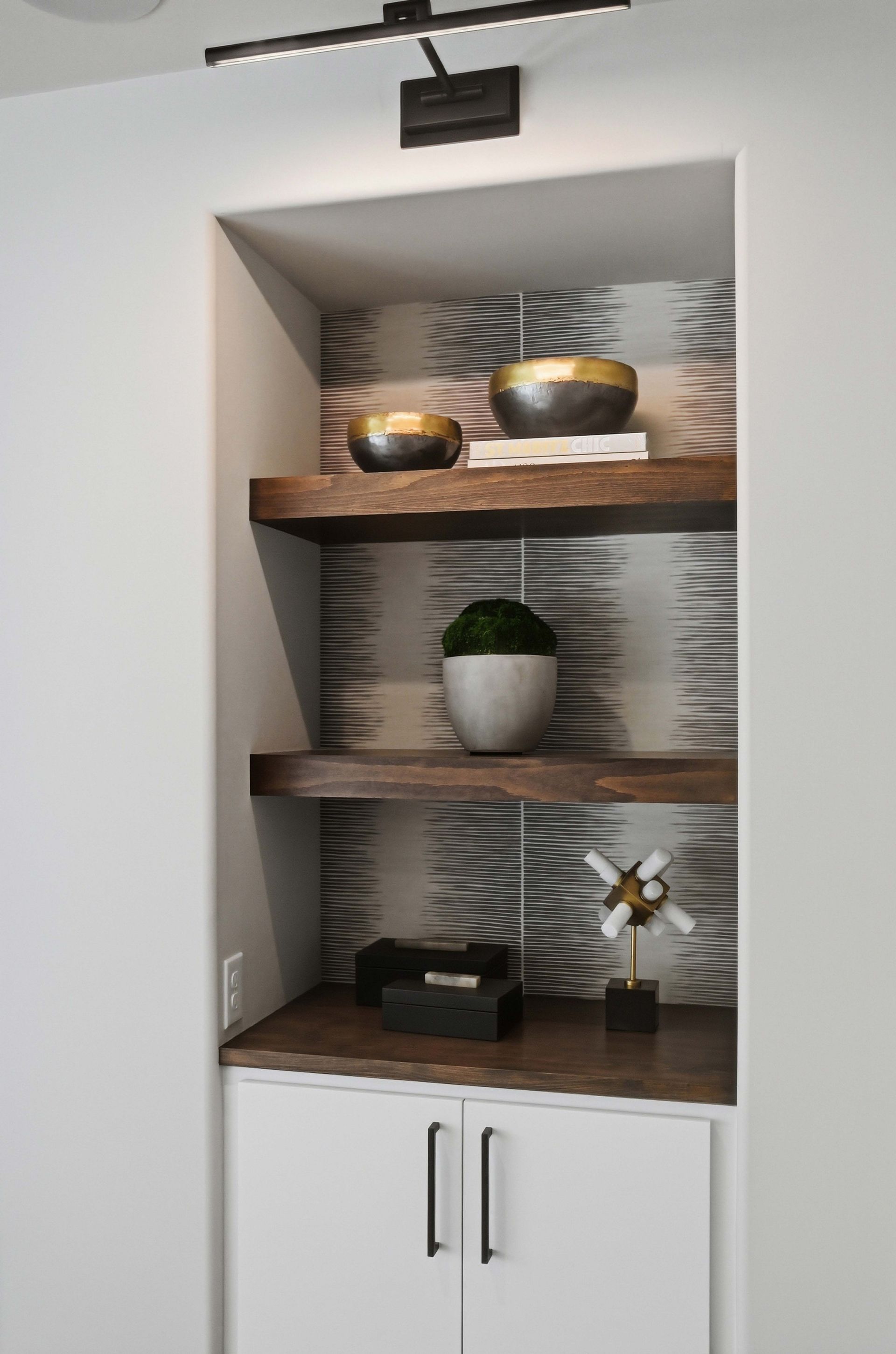 Built-in wall niche with wooden shelves, decor bowls, a potted plant, and cabinets below
