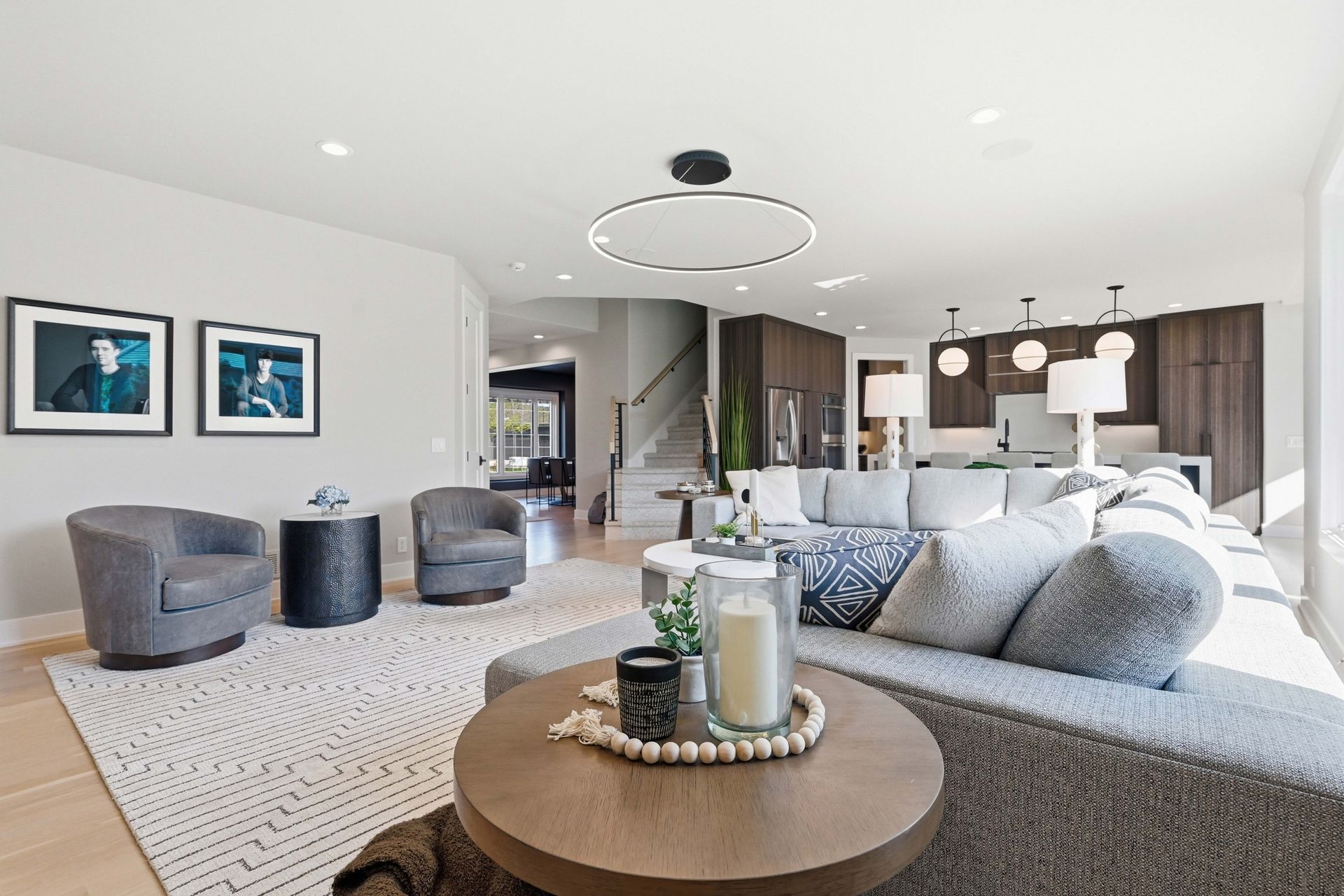 Bright modern living room with gray furniture, patterned rug, round coffee table, and open kitchen in background