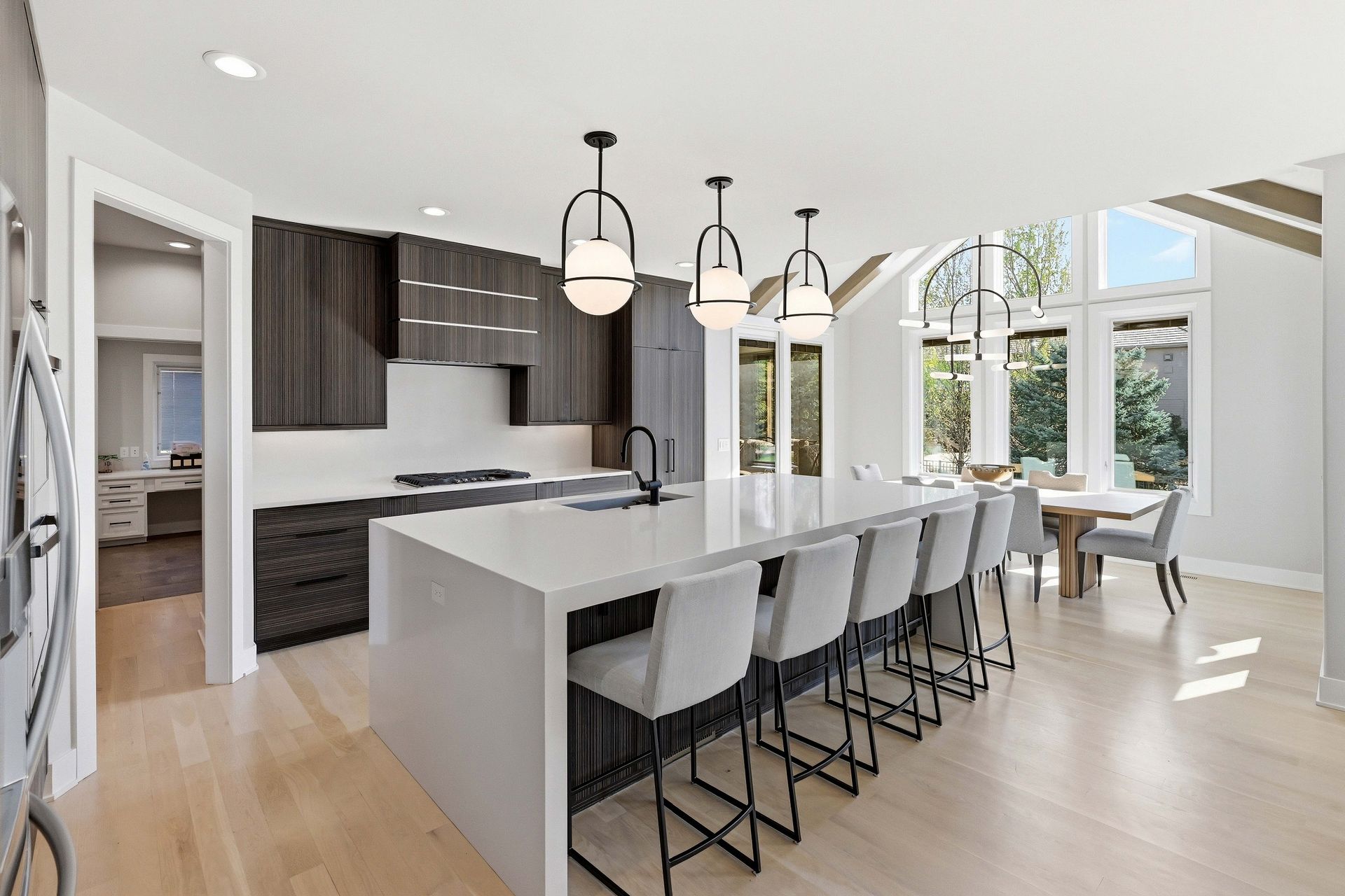 Modern white kitchen with island, pendant lights, bar stools, and large windows overlooking trees