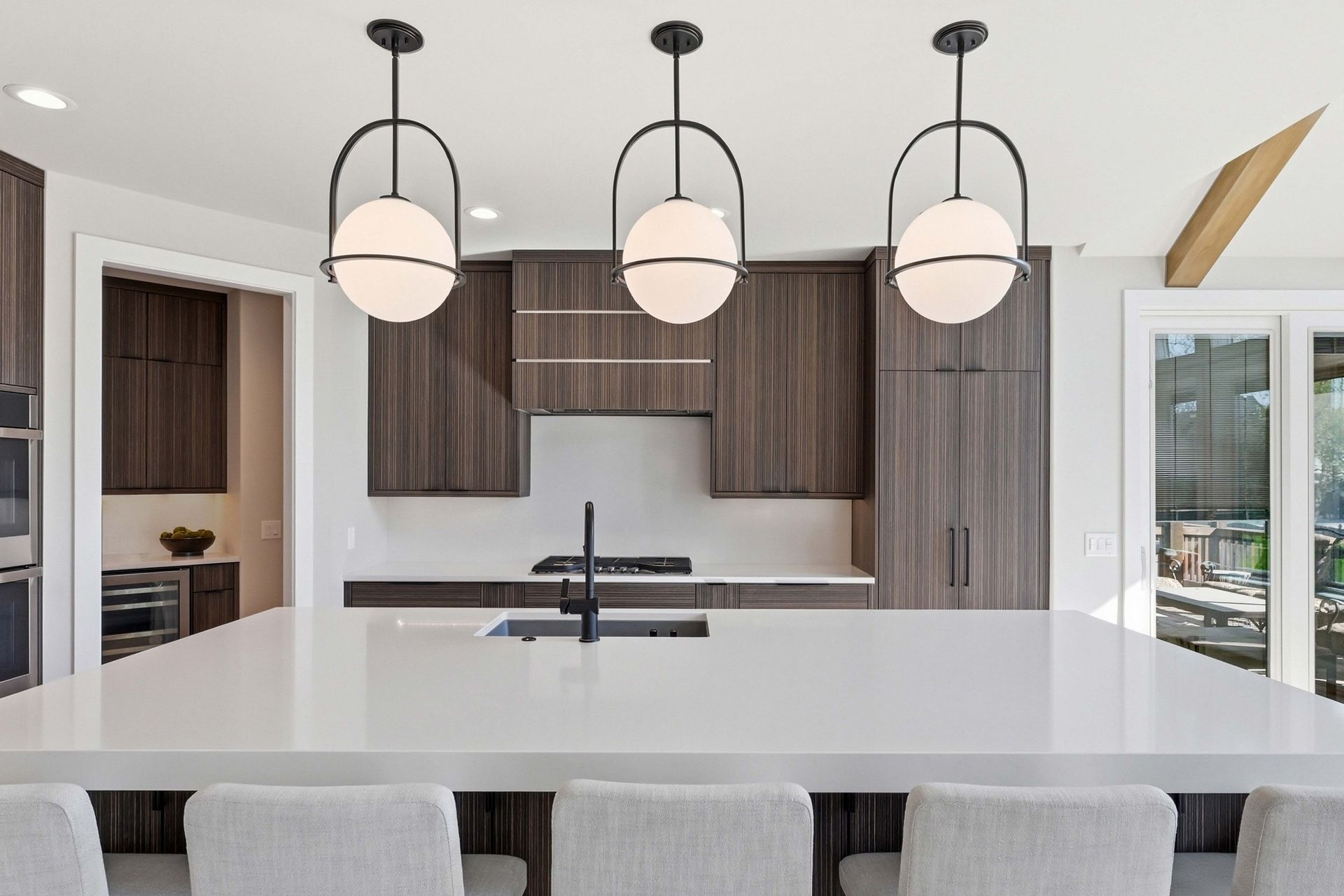 Modern kitchen with a large white island, three pendant lights, and dark wood cabinetry