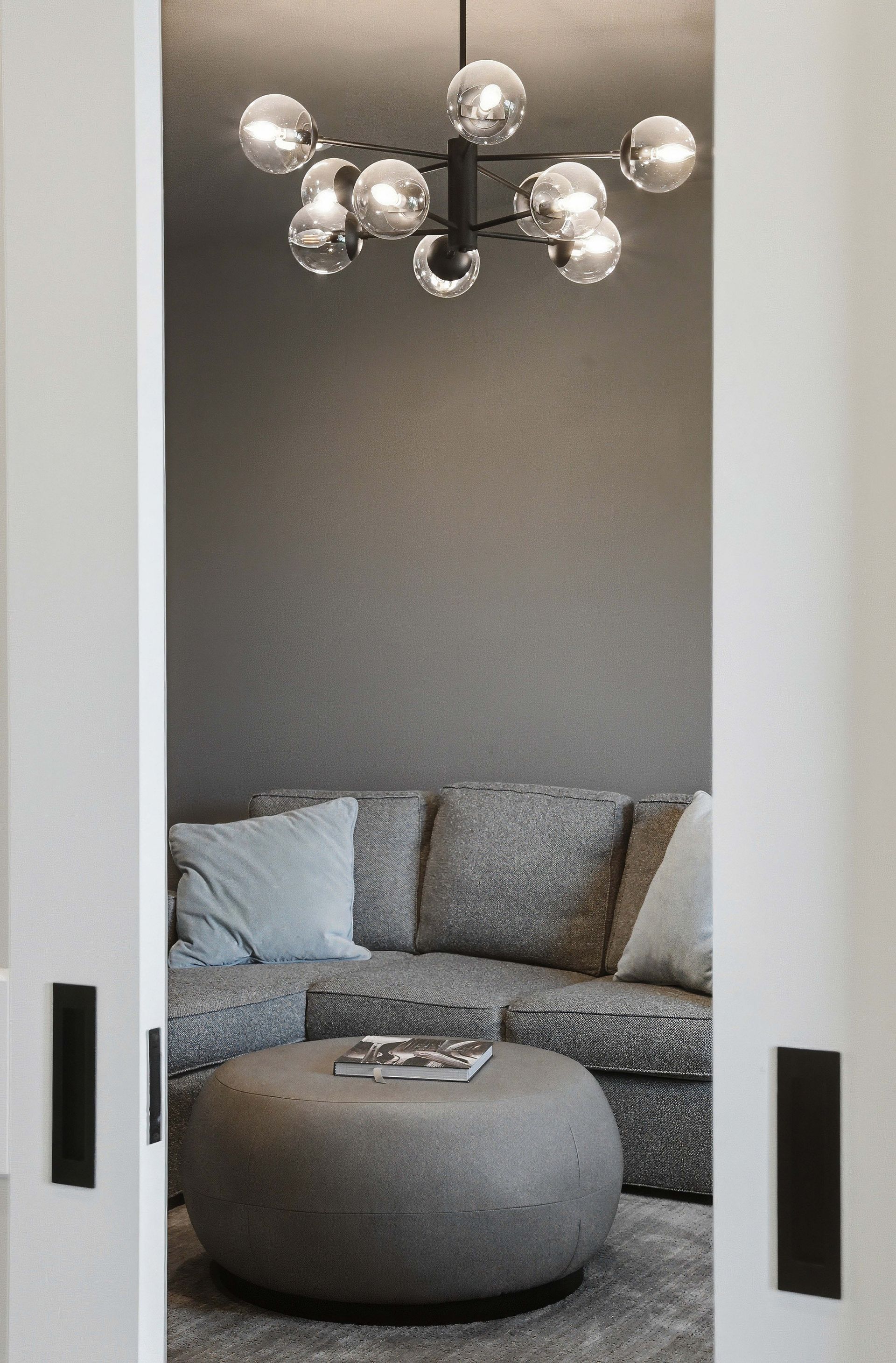 Cozy gray lounge nook with a curved sofa, round ottoman, and modern chandelier