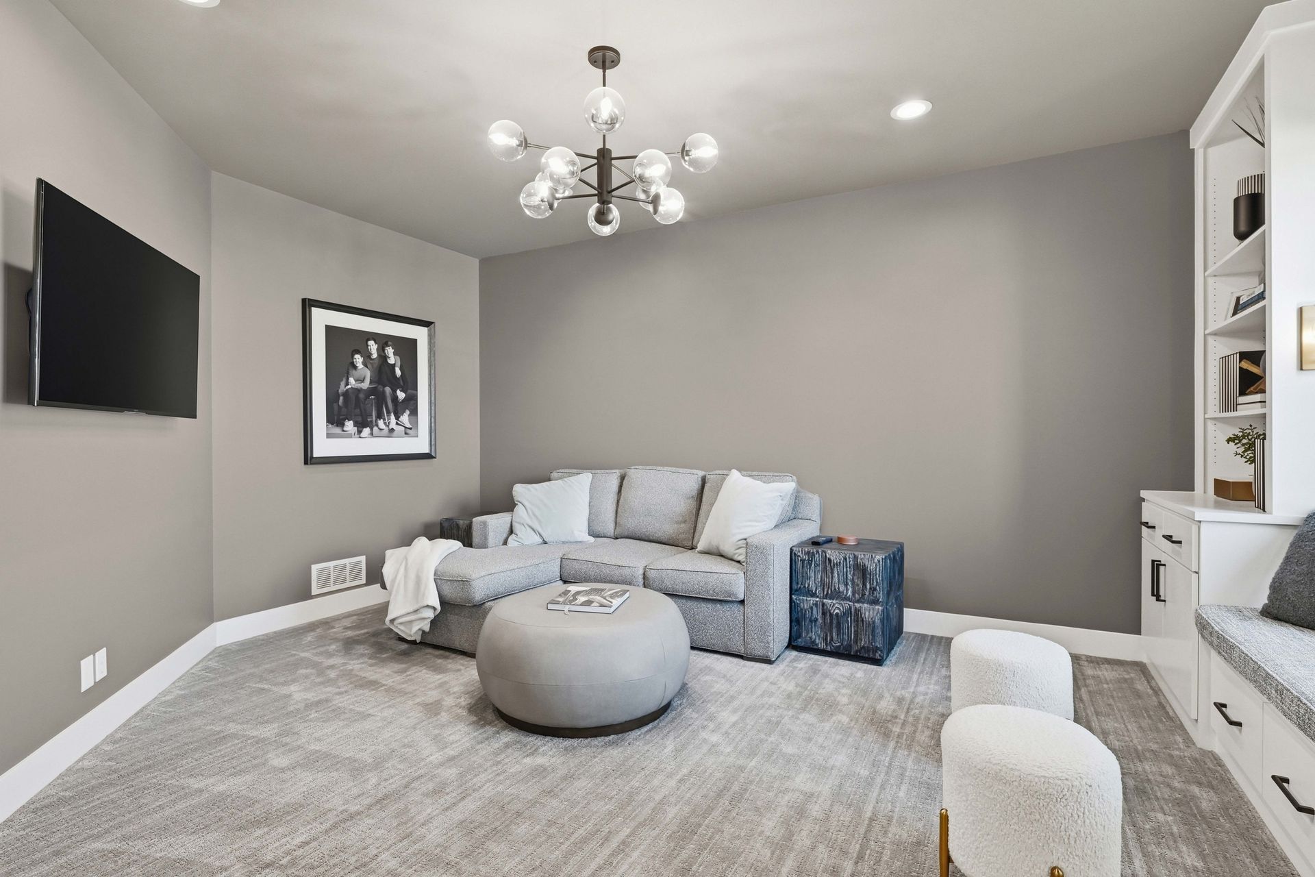 Modern gray living room with sectional sofa, ottoman, wall-mounted TV, and built-in shelving