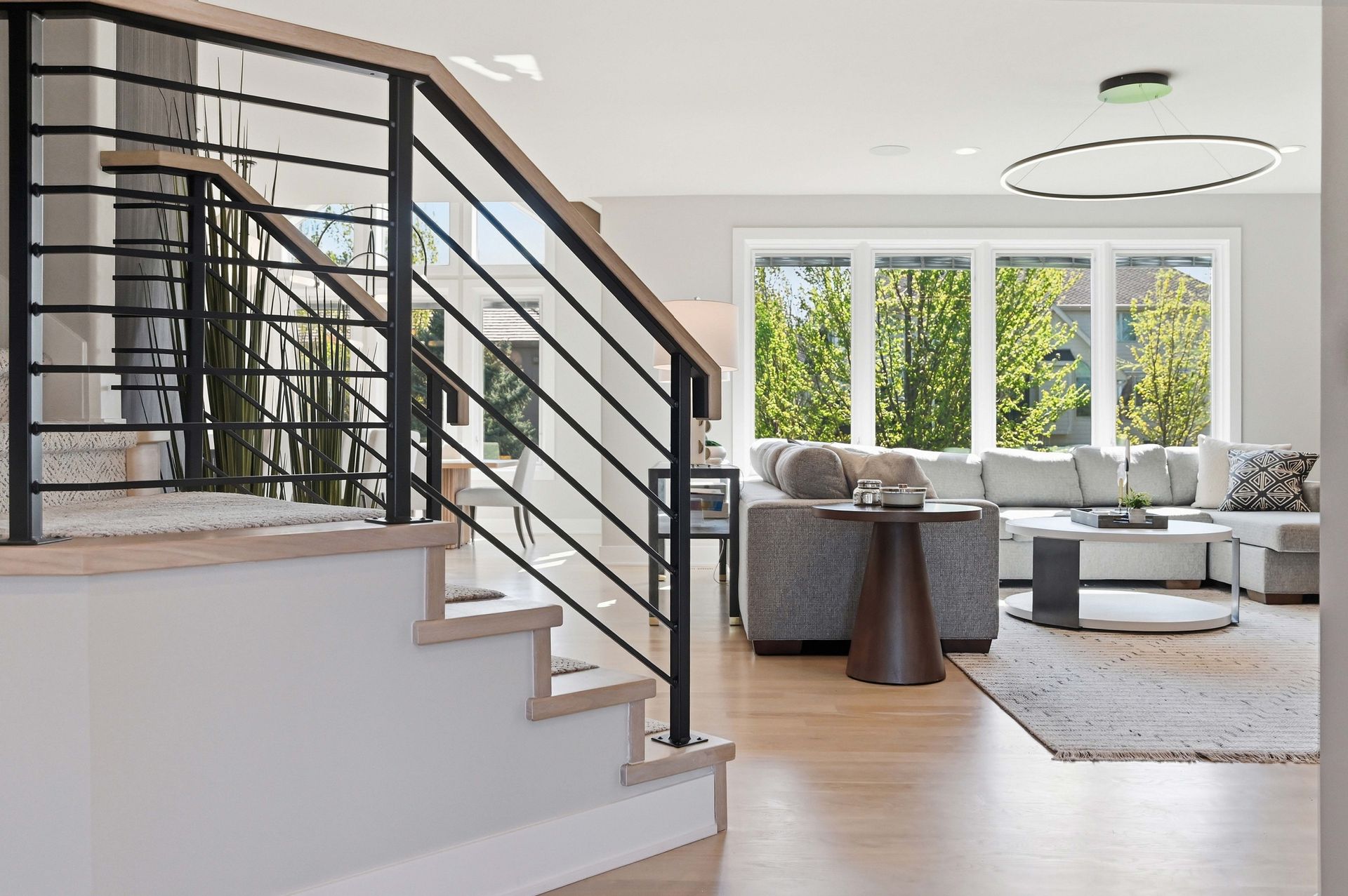 Modern living room with gray sectional, large windows, and black metal staircase railing
