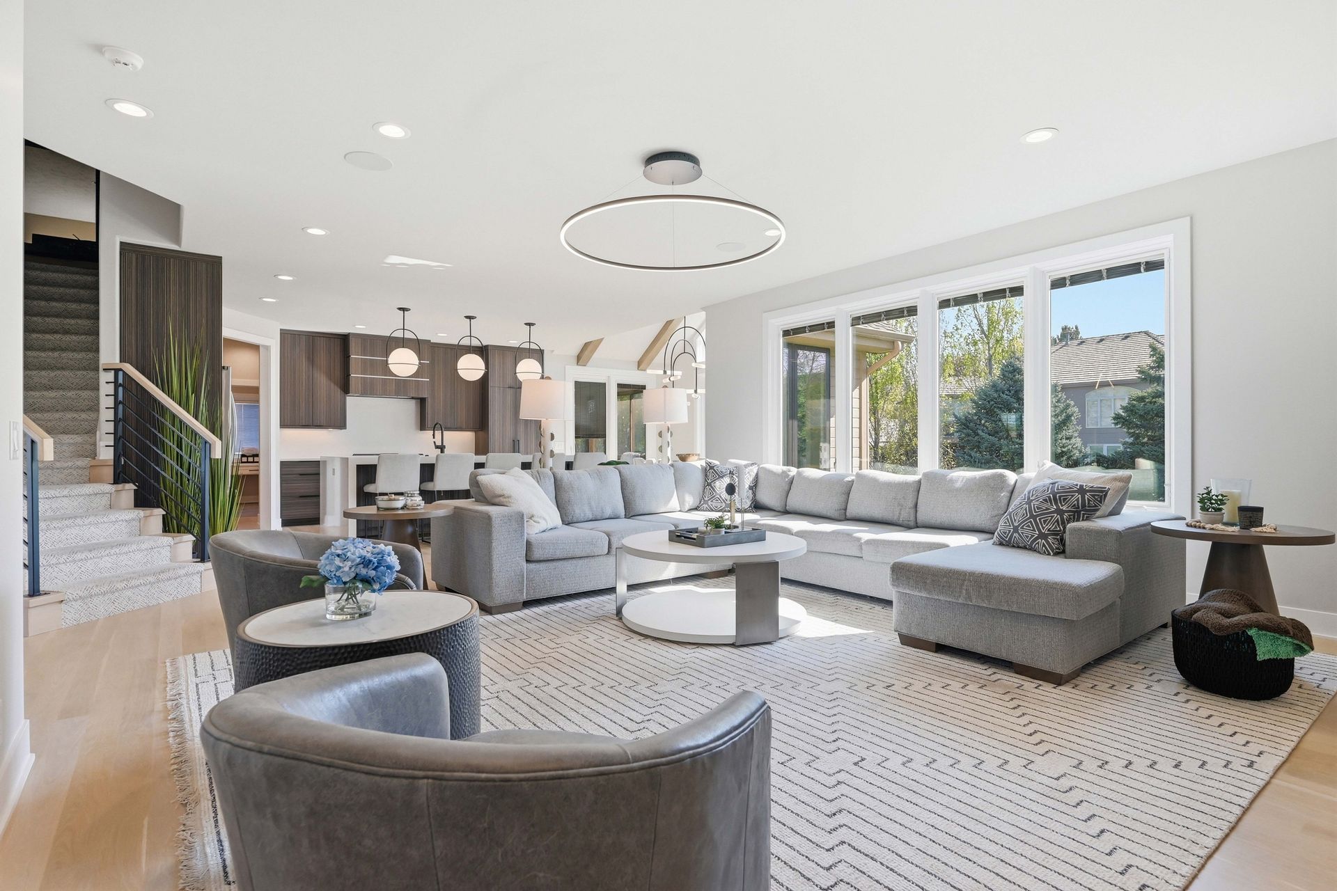 Bright modern living room with gray sectional sofas, large windows, and a white patterned rug