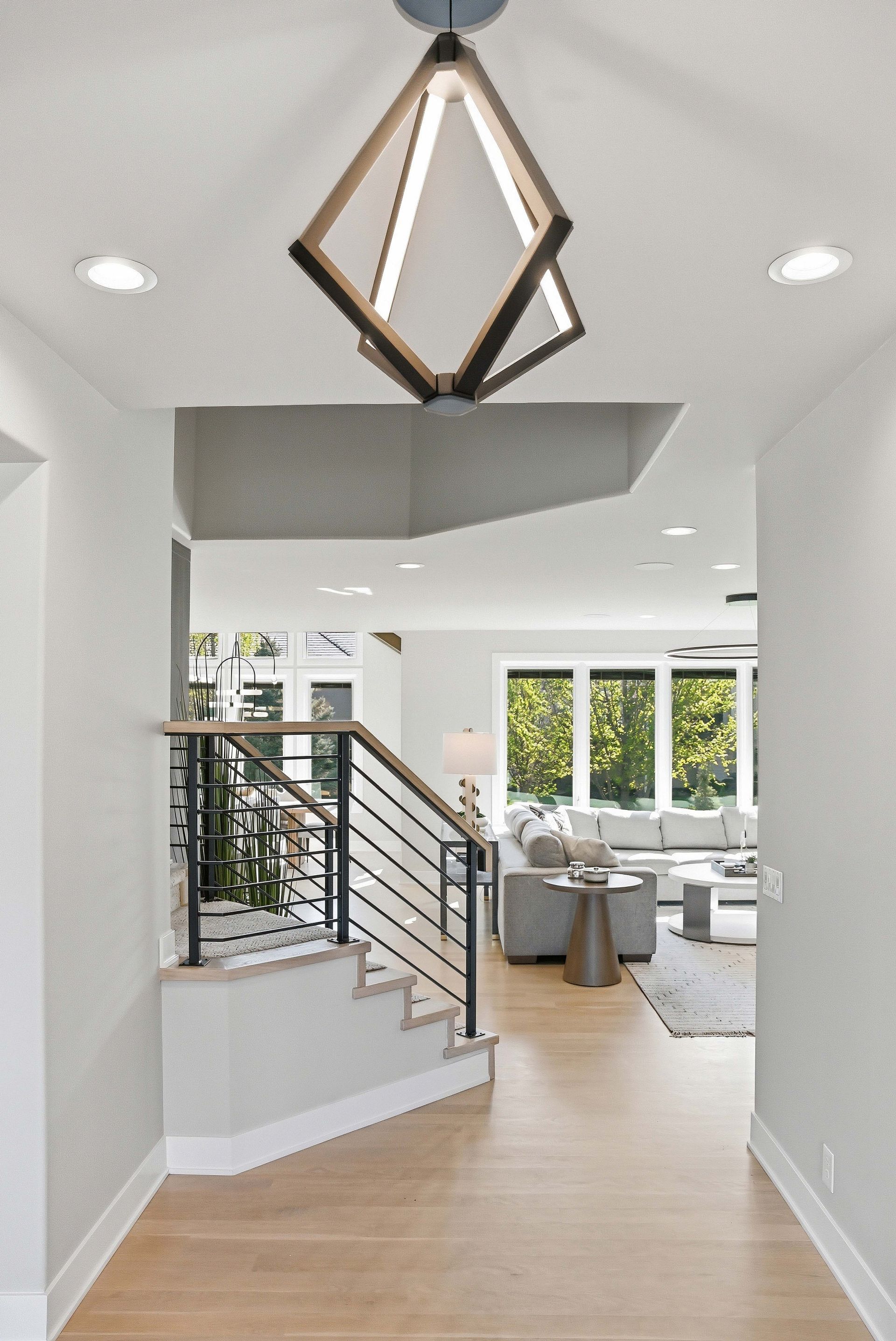 Modern foyer with staircase, geometric pendant light, and open view to a bright living room.