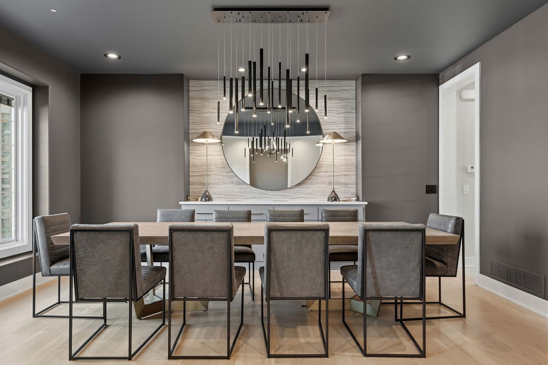 Modern dining room with long table, six chairs, large mirror, and black pendant light over a stone accent wall