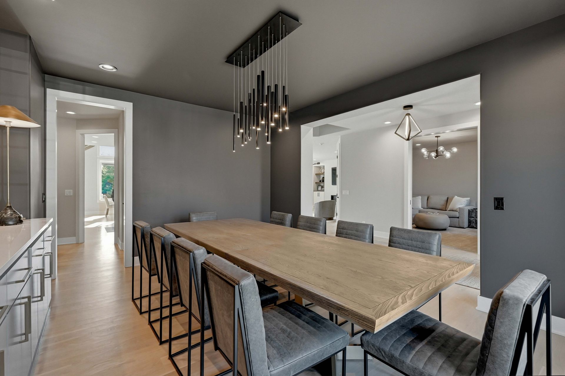 Modern kitchen with long wood table, black barstools, and gray walls opening to a living room