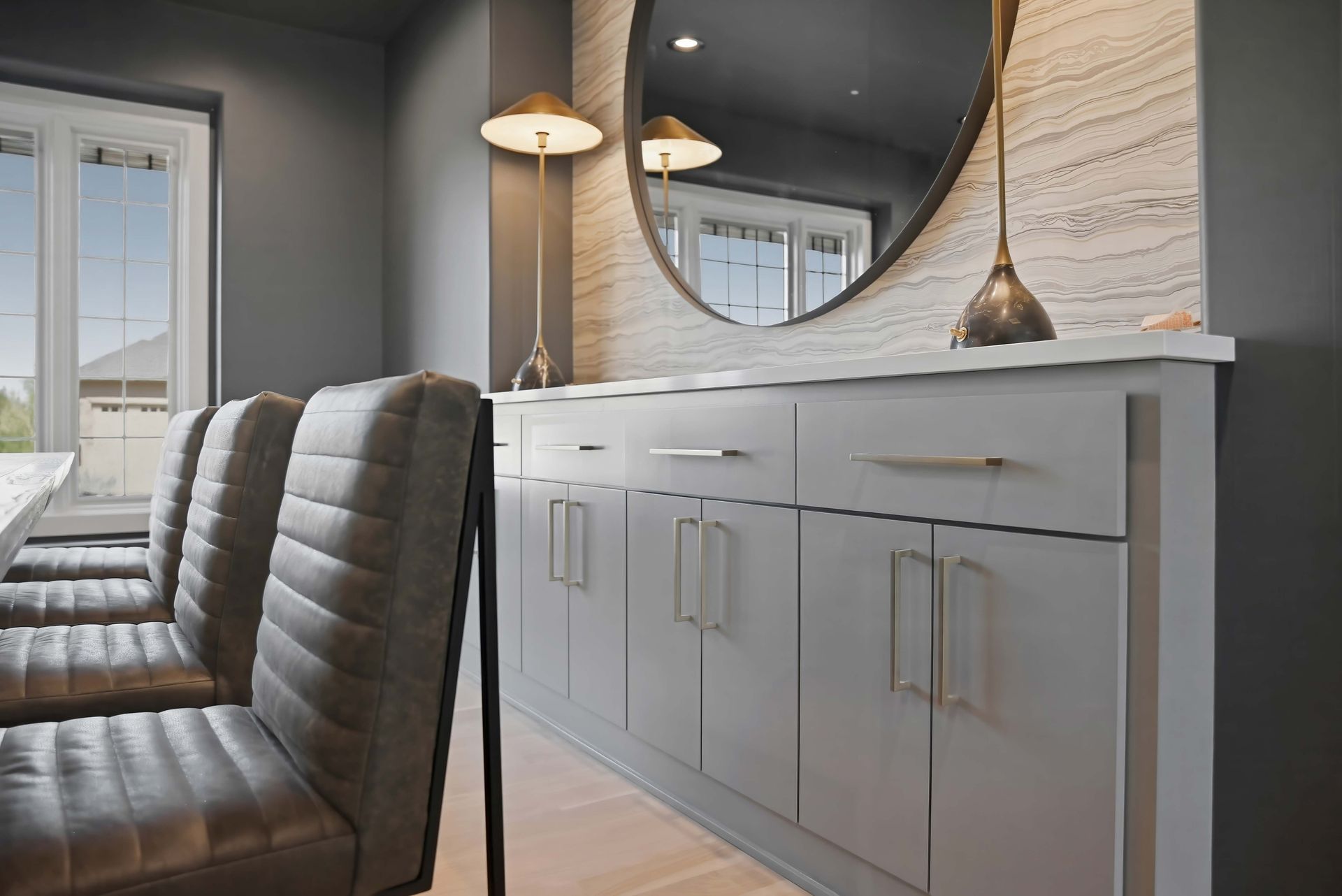 Modern dining area with gray chairs, white sideboard, round mirror, and pendant lights
