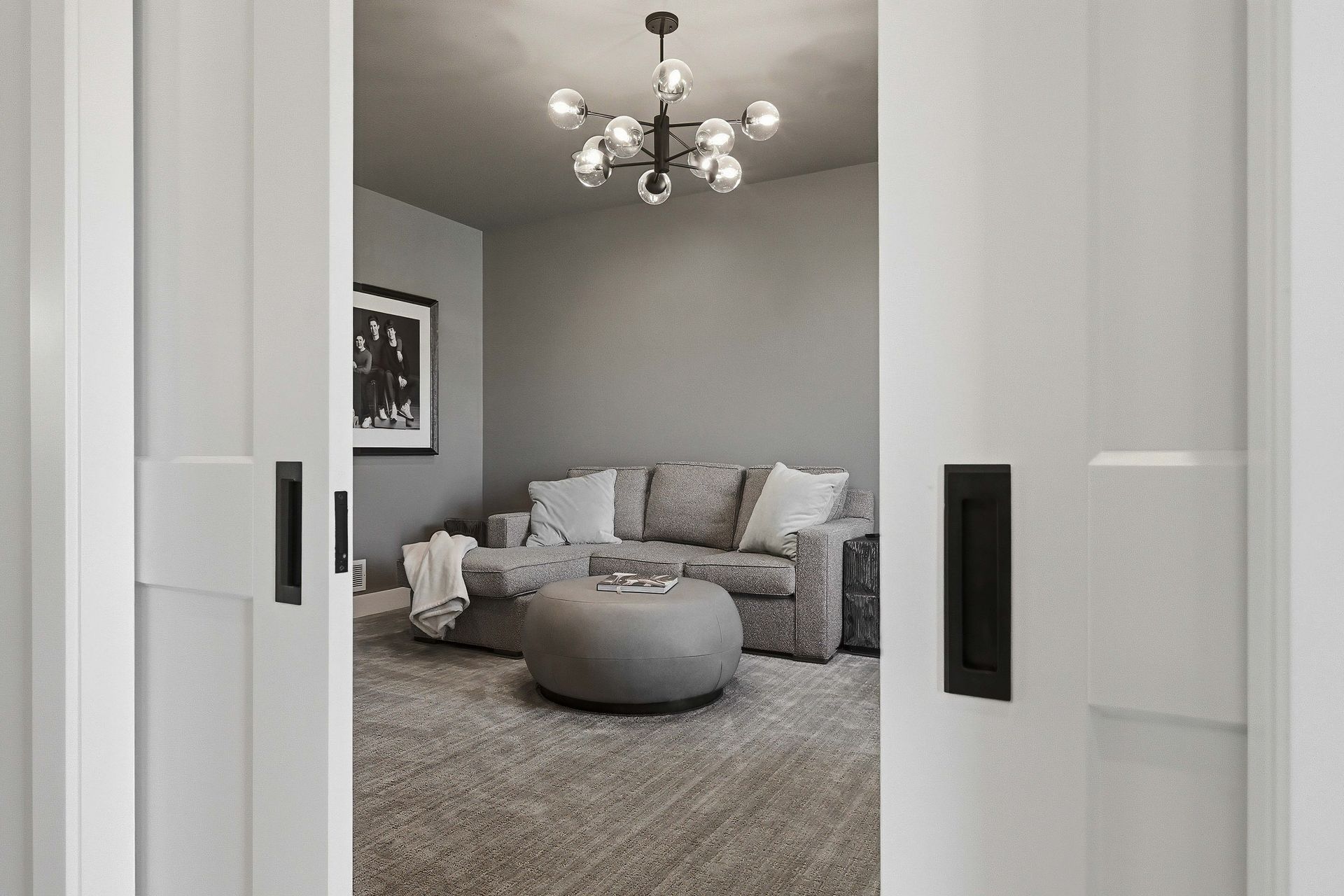 View through sliding doors into a gray living room with a chandelier and round ottoman