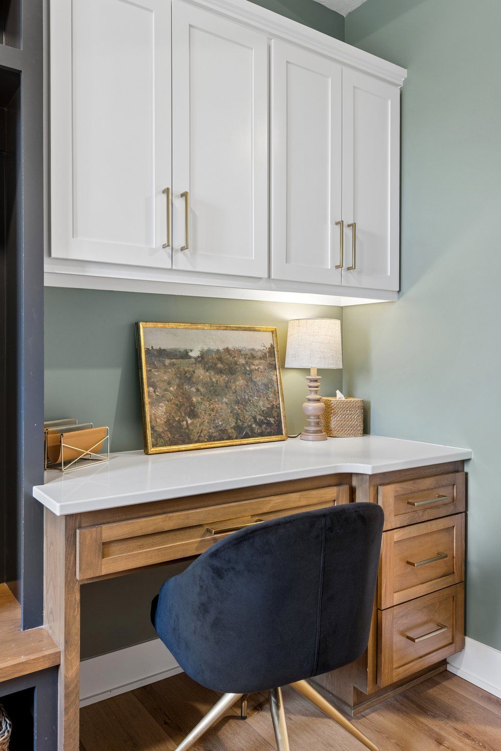 Home office desk with white cabinets, wood drawers, a lamp, and a navy chair against a green wall