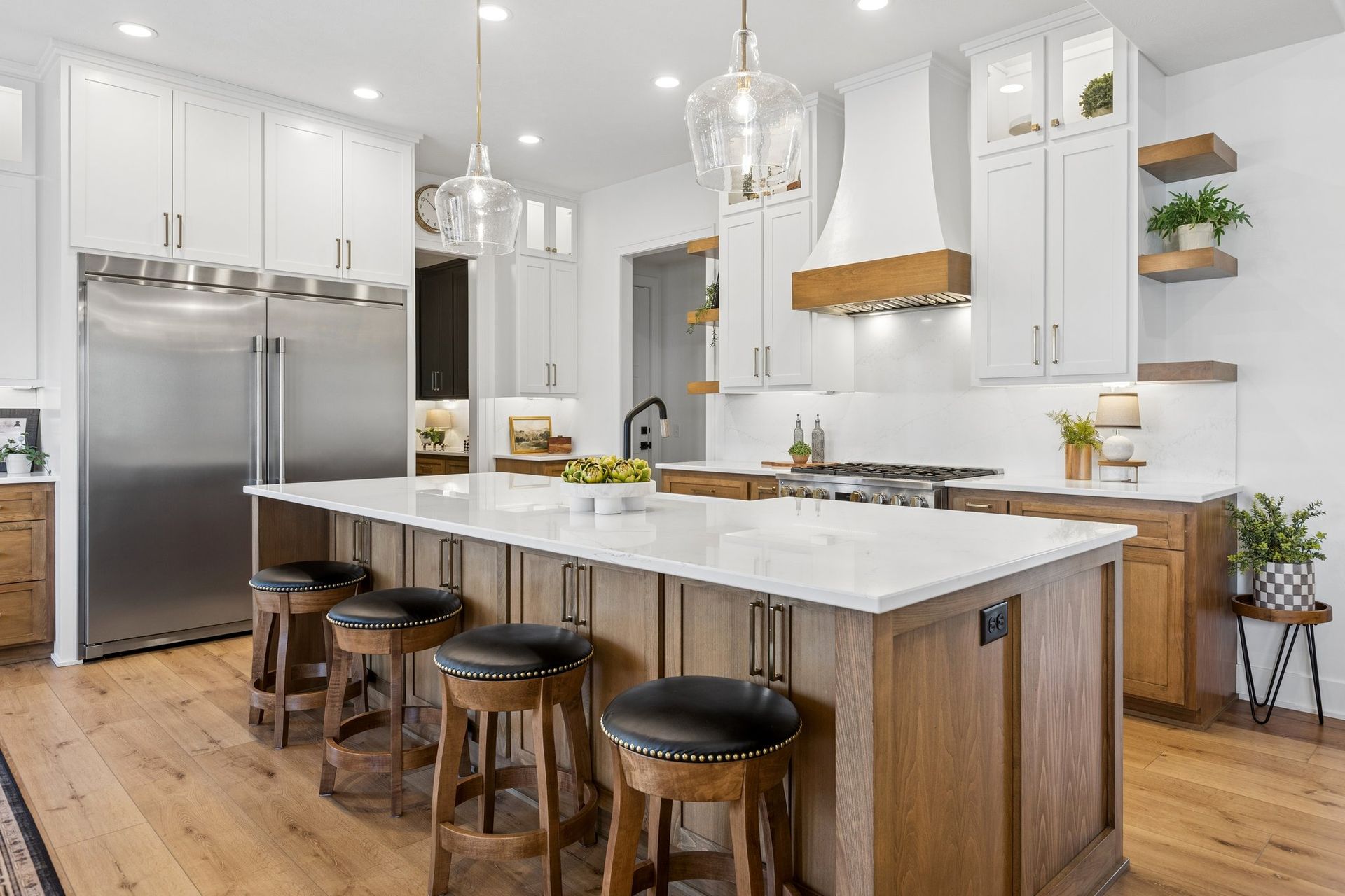 Modern white kitchen with a large island, stainless steel appliances, and four wooden stools