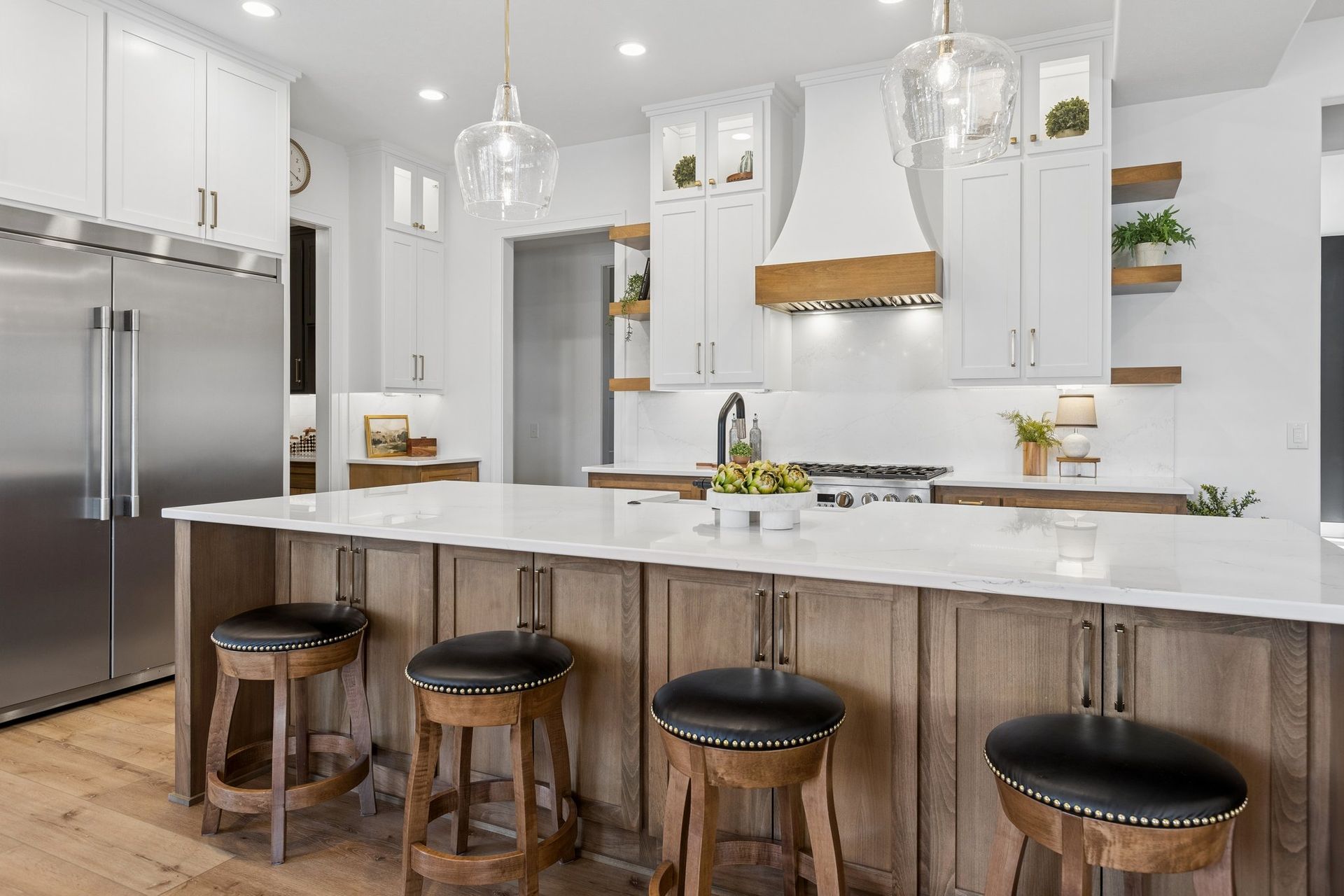 Modern white kitchen with stainless fridge, island, and four wooden stools